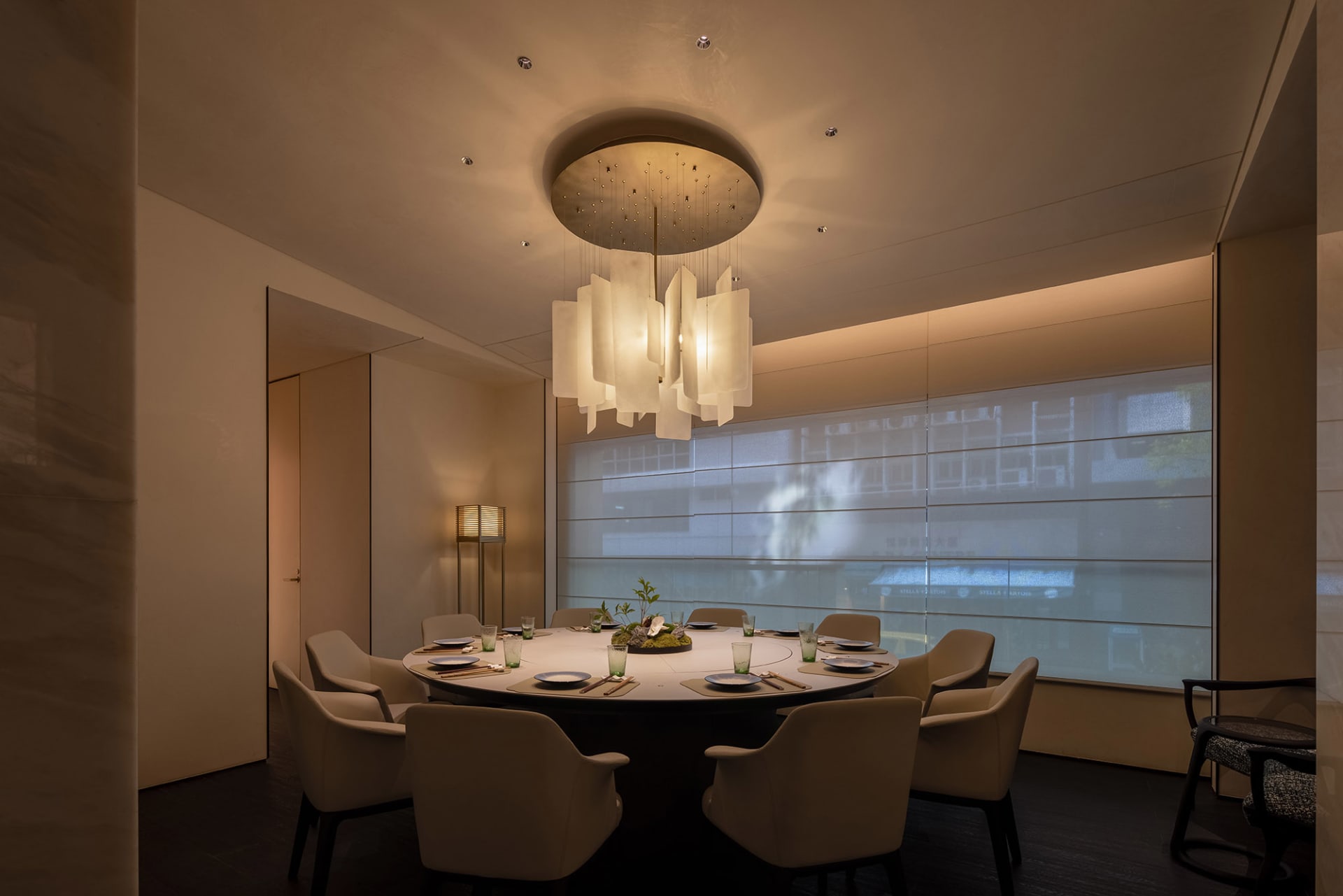 A modern dining room with a round table, white chairs, and a unique pendant light.