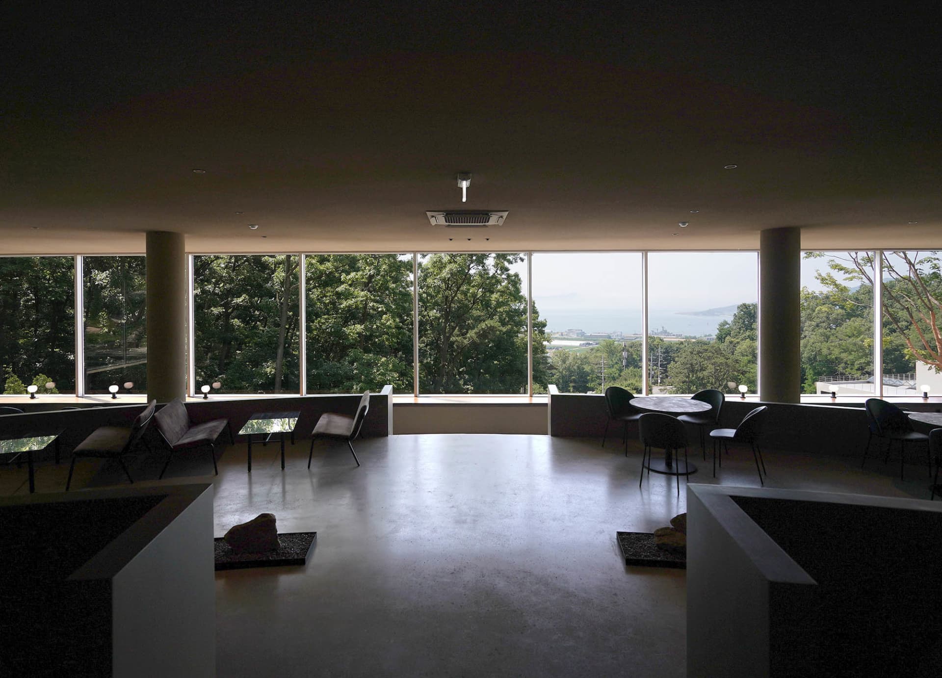 Modern restaurant interior with extensive glass window walls providing ample sunlight and a glimpse of the sea and lush green
