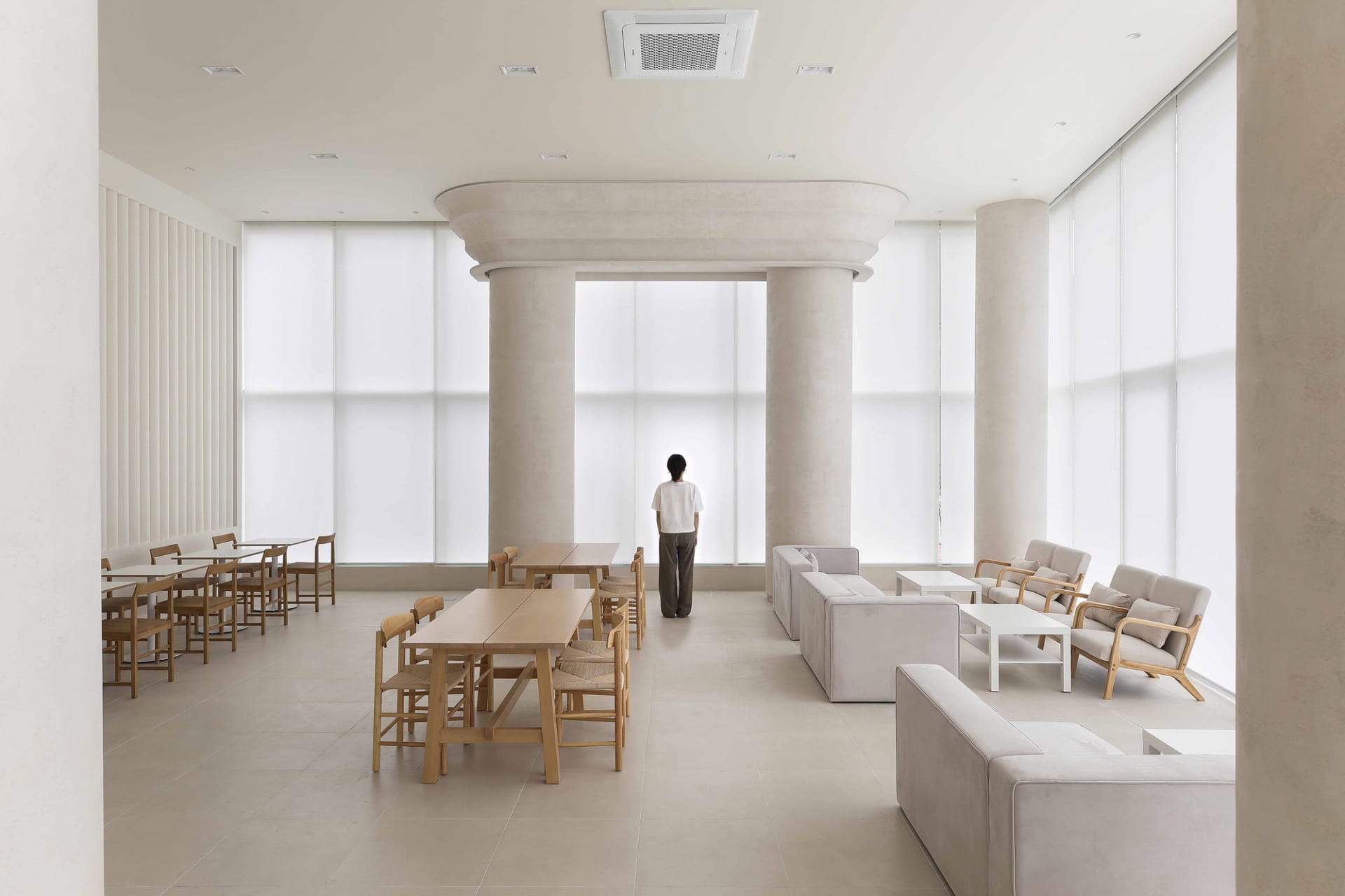 A modern waiting area featuring concrete flooring, minimalist furniture, and large windows with vertical blinds.