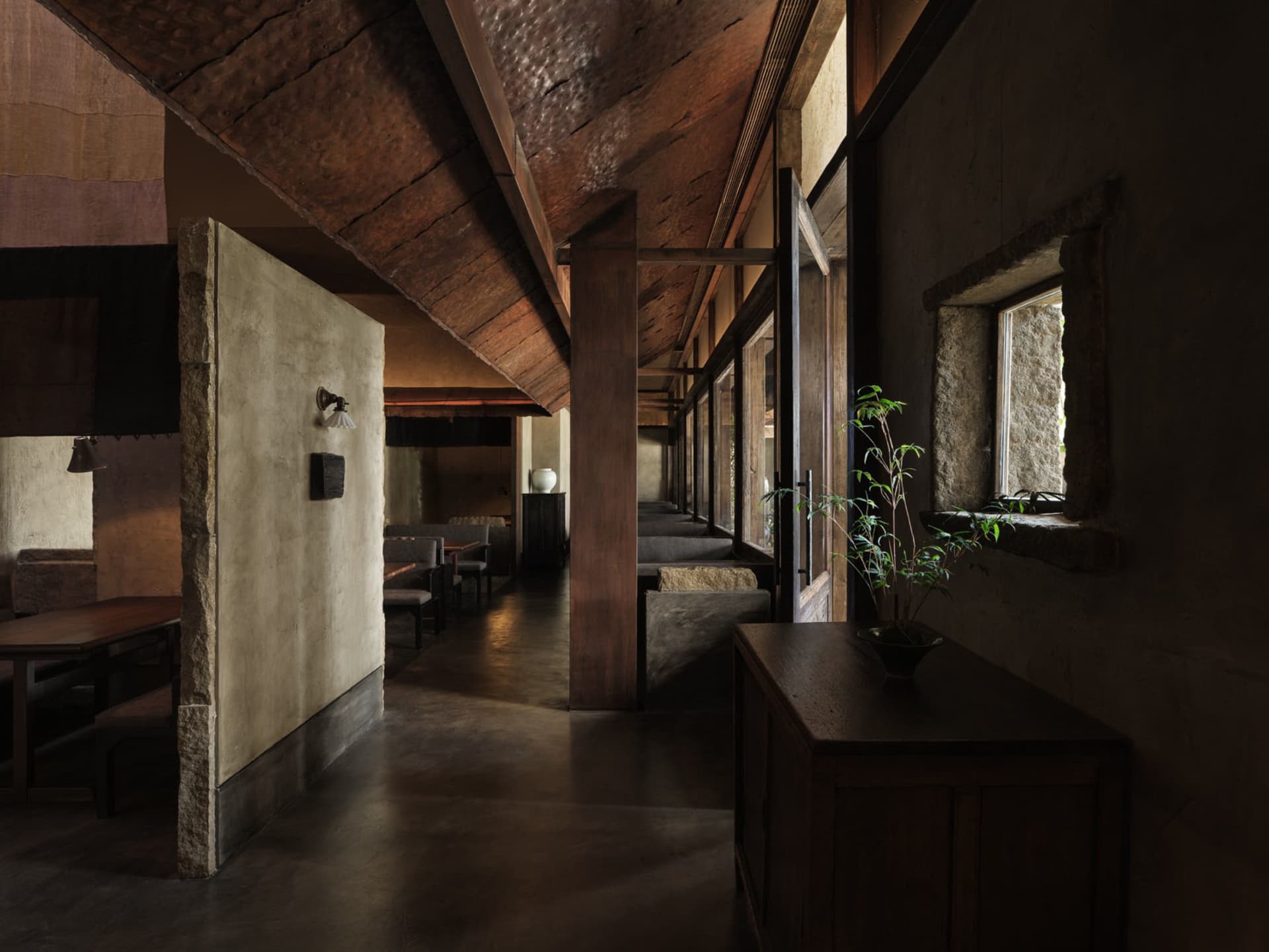 A hallway with concrete walls, wooden beams, and a plant on a side table.