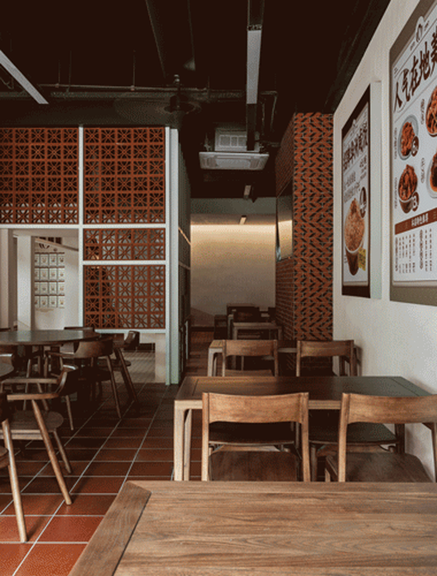 A photograph of an industrial restaurant interior with wooden tables and chairs, brick wall, and menu board on the wall.