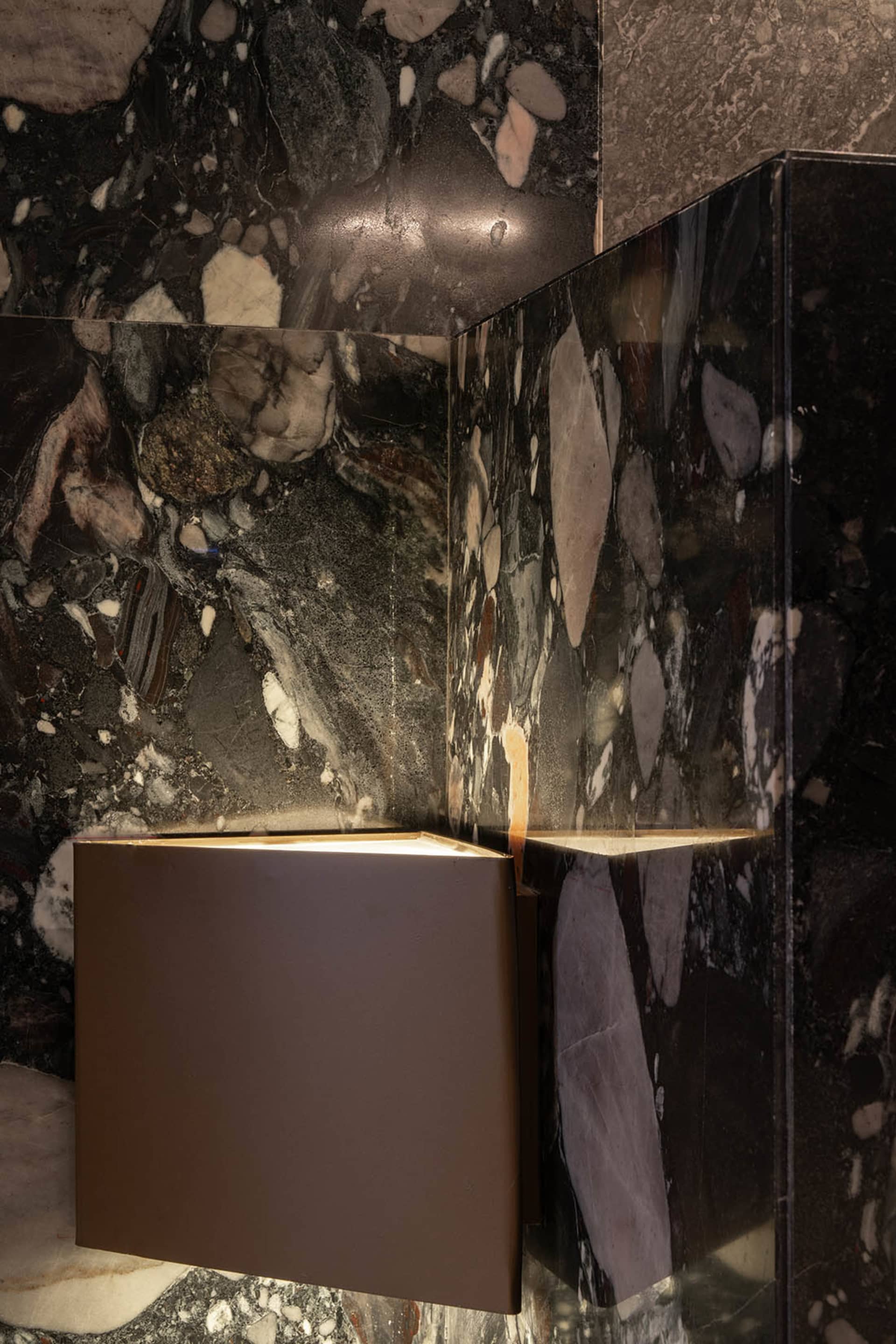 A modern interior space featuring marble walls with illuminated lighting fixtures.