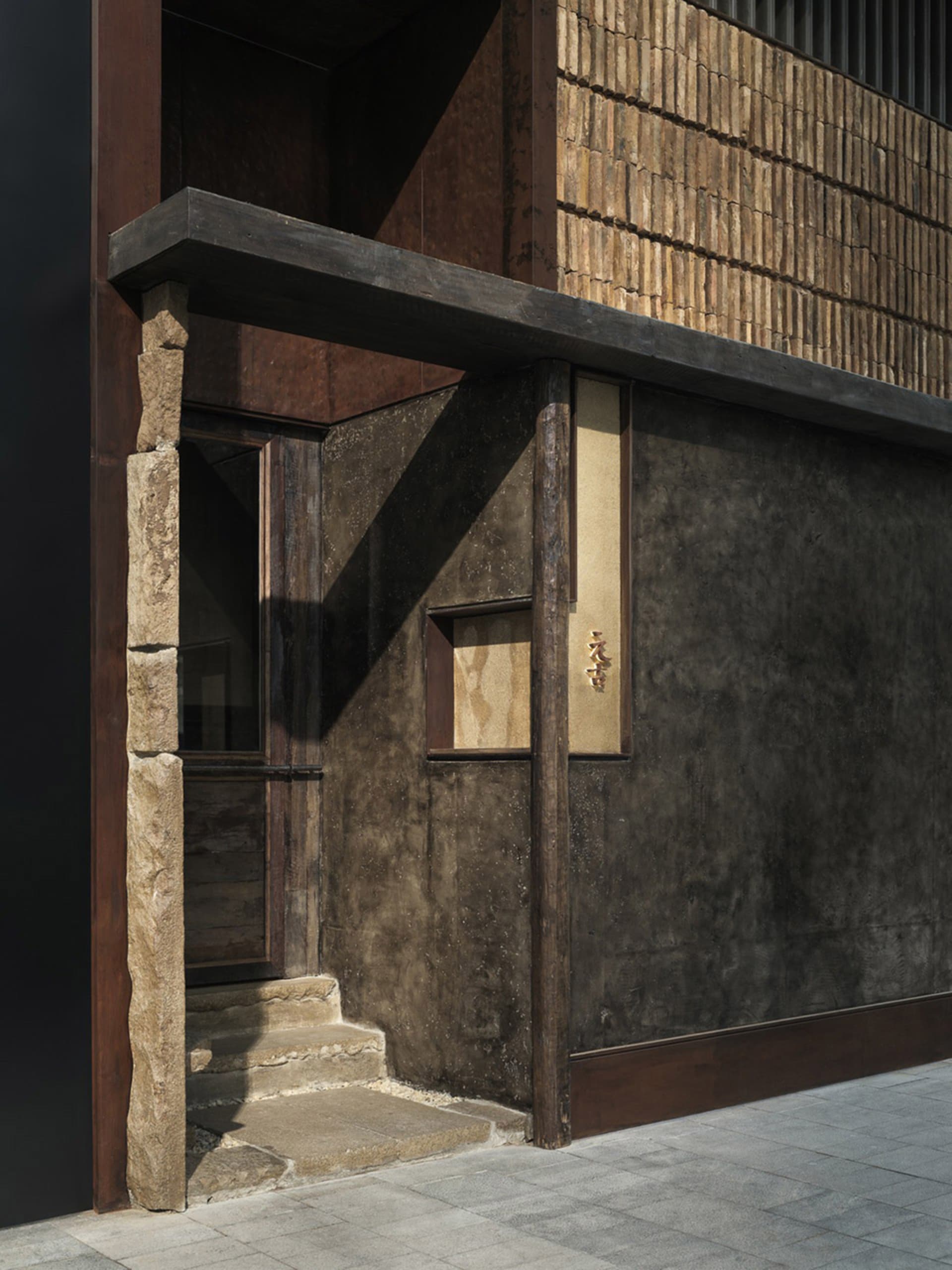An exterior view of a retail storefront featuring reclaimed concrete, wood, and brick materials.