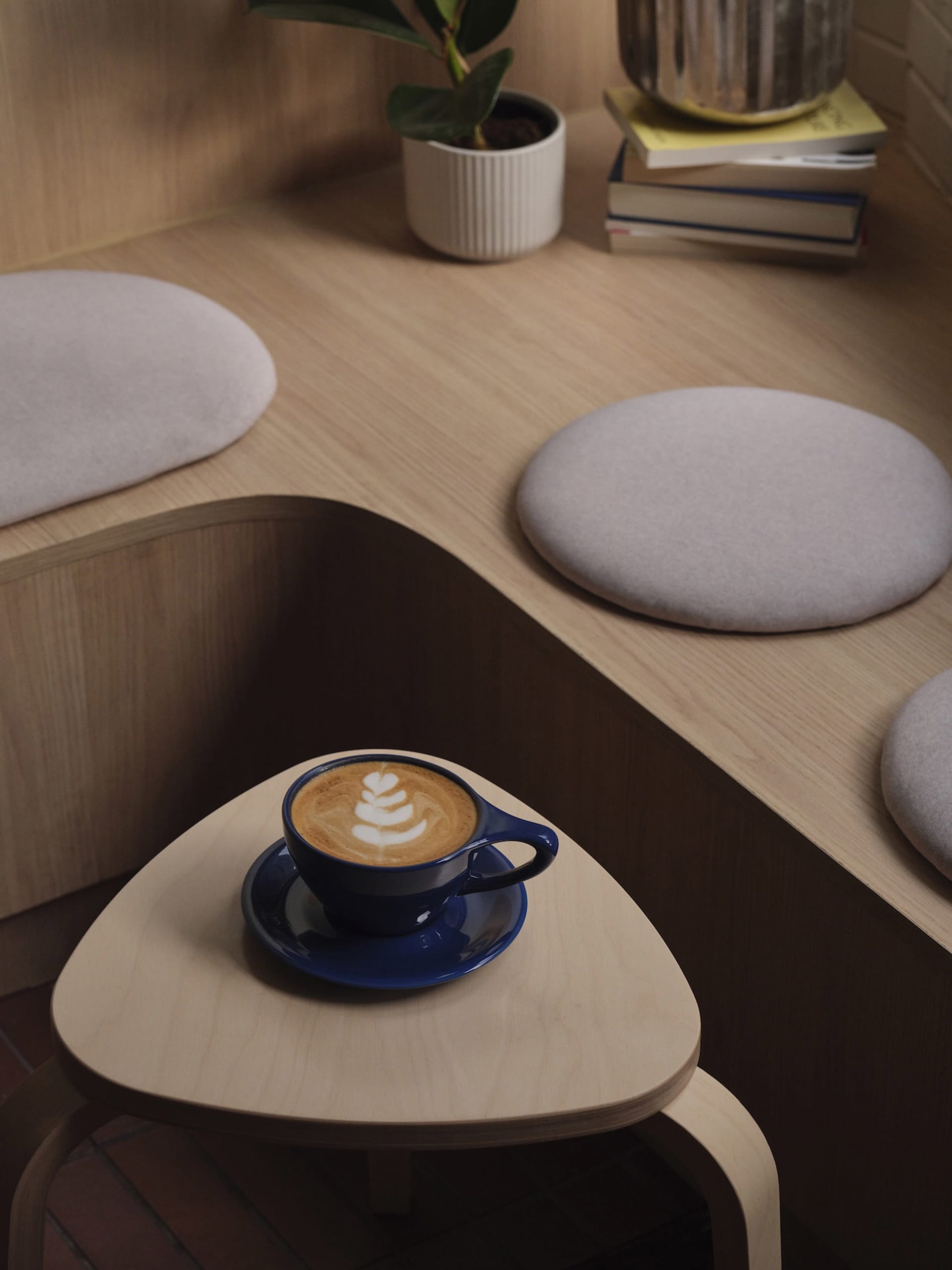 A cozy coffee shop interior with a wooden table featuring a blue ceramic coffee cup with latte art, surrounded by upholstered