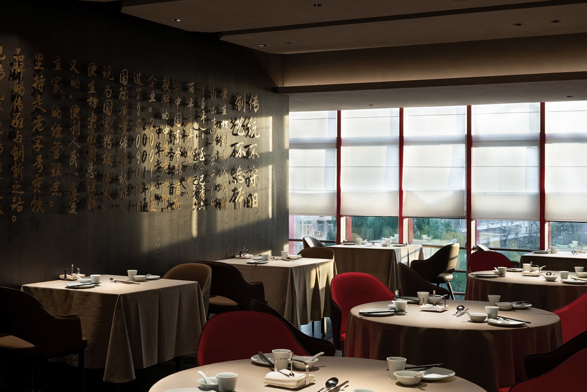 A restaurant interior featuring decorative Chinese calligraphy on the walls, round tables with tableware, and red chairs.