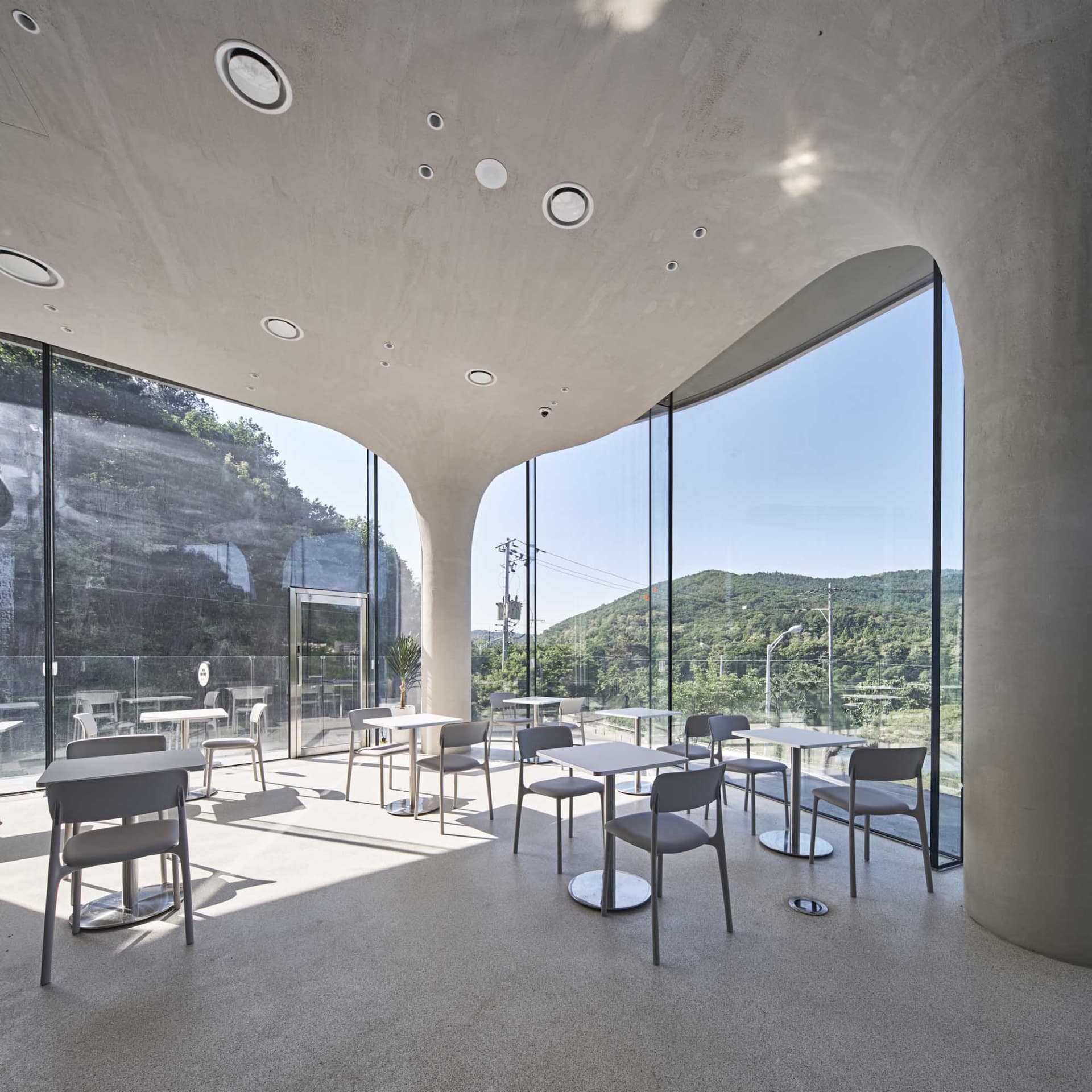 A modern cafe interior featuring glass and concrete materials, with seating and tables designed for functionality and aesthet