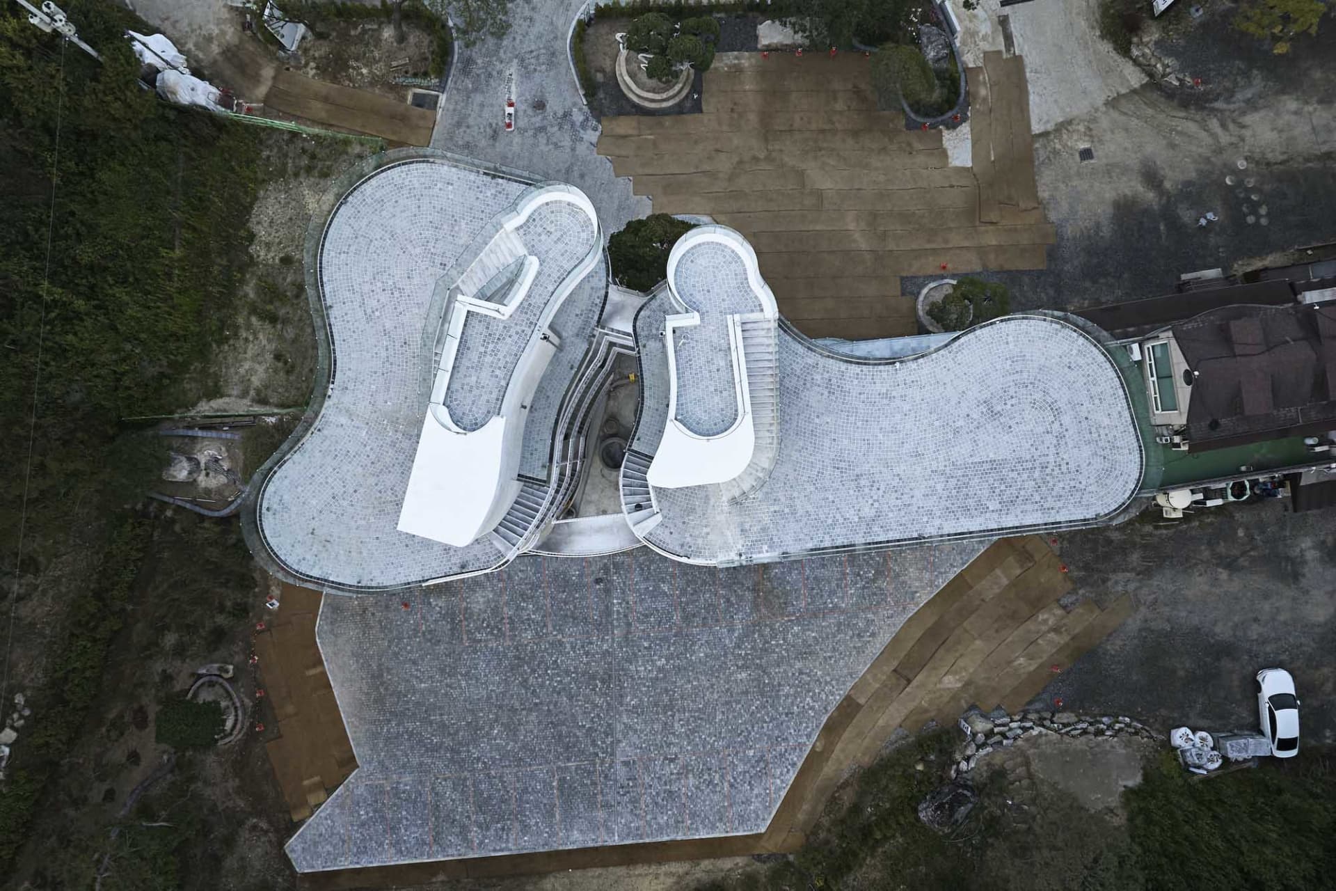 An aerial view of a modern public viewpoint pavilion with a tiled walkway and open seating area.