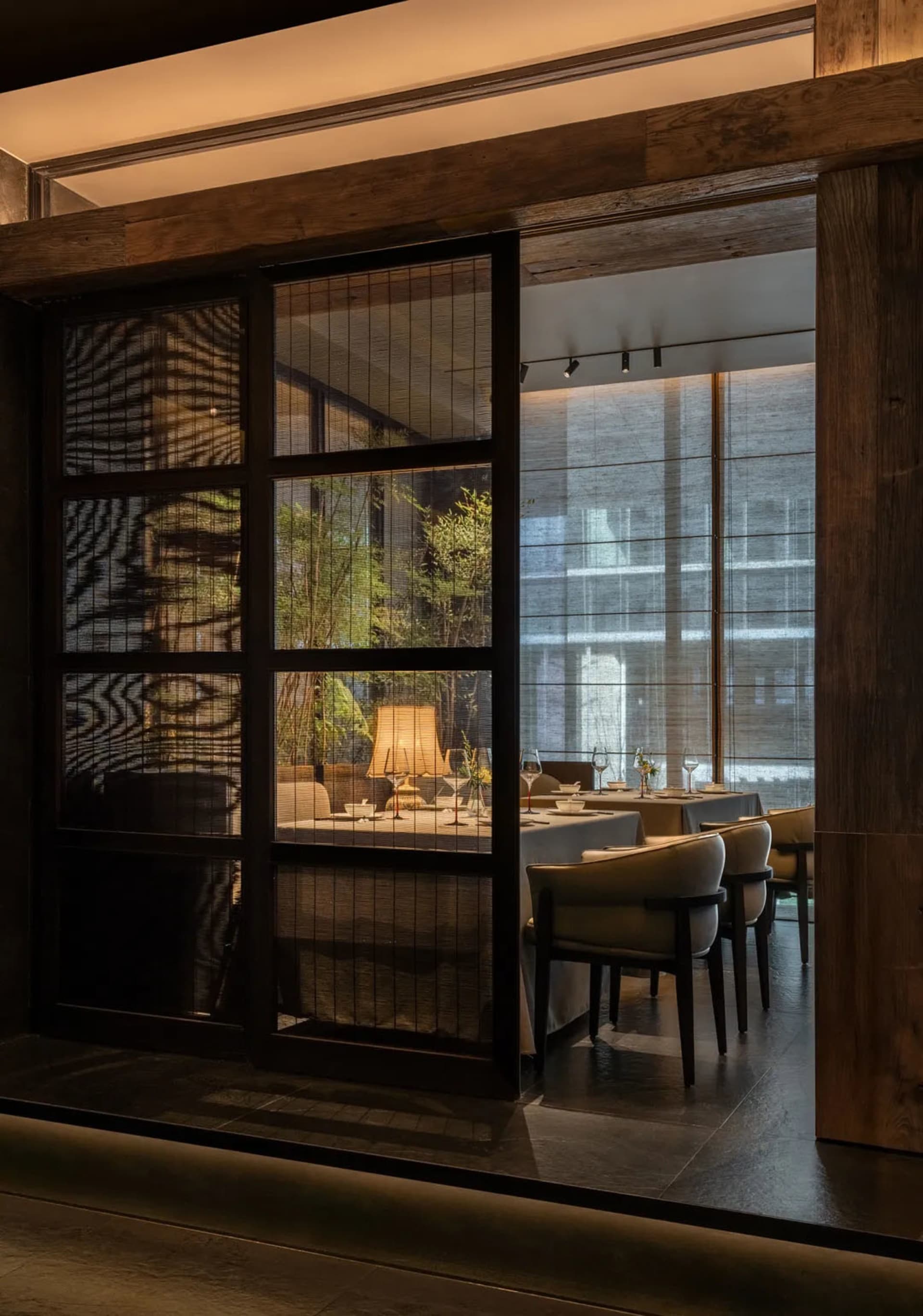A modern restaurant interior with wooden tables, glass walls, and minimalist decor.