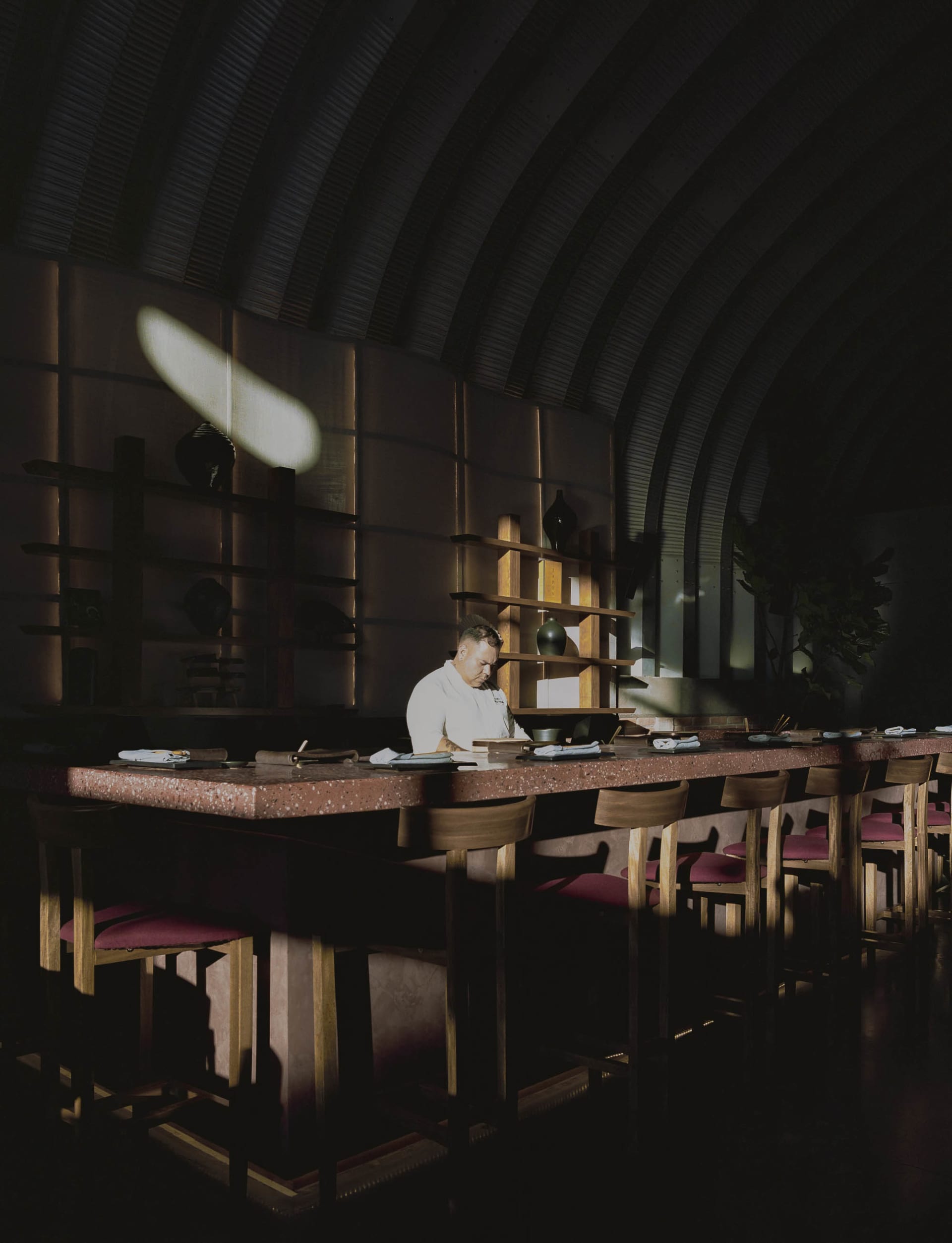 A chef preparing food behind a terrazzo counter in a restaurant interior with a dark, minimalist design.