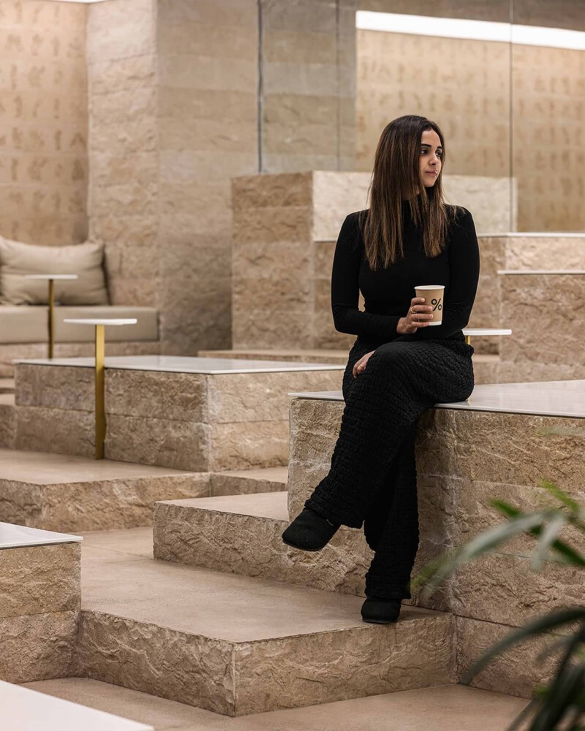 A woman sitting in a modern stone cafe space with a coffee cup in her hand.