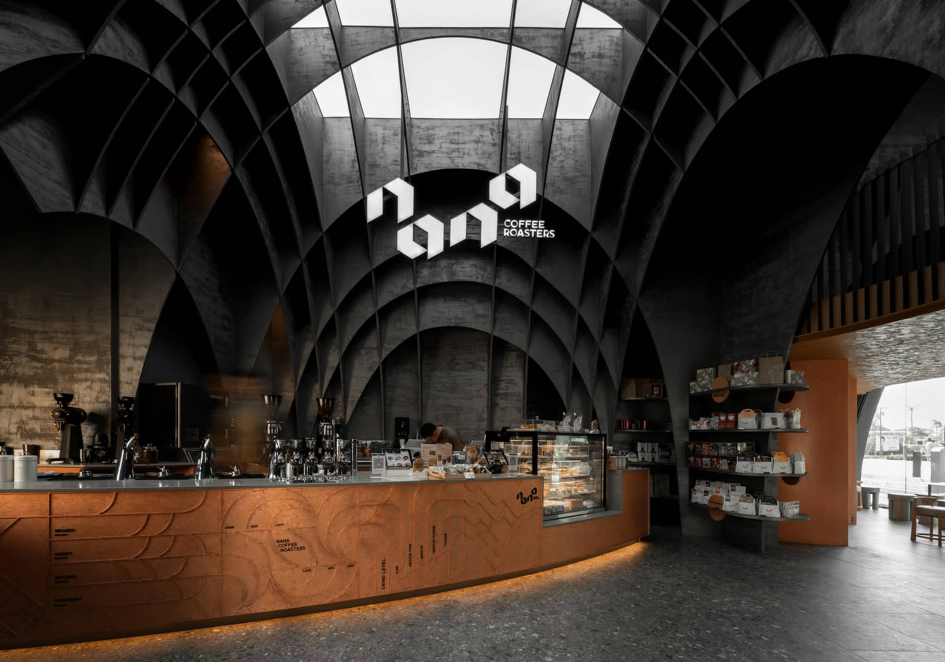 A modern, industrial-style coffee shop with a concrete counter featuring a logo for a coffee roasters brand below it.