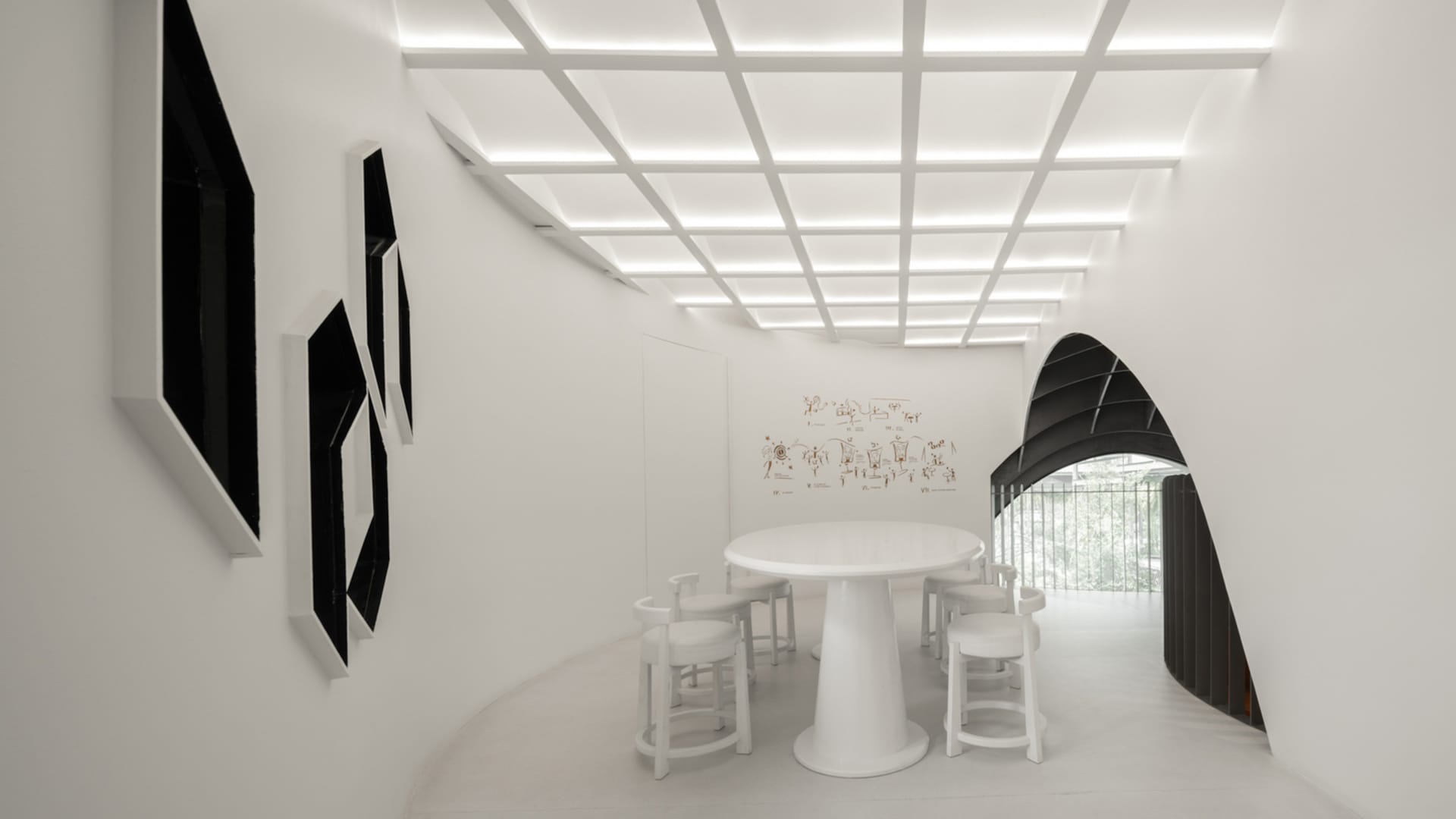 White minimalist interior design of a restaurant/cafe with a round white table, white stools, and framed black artwork on whi