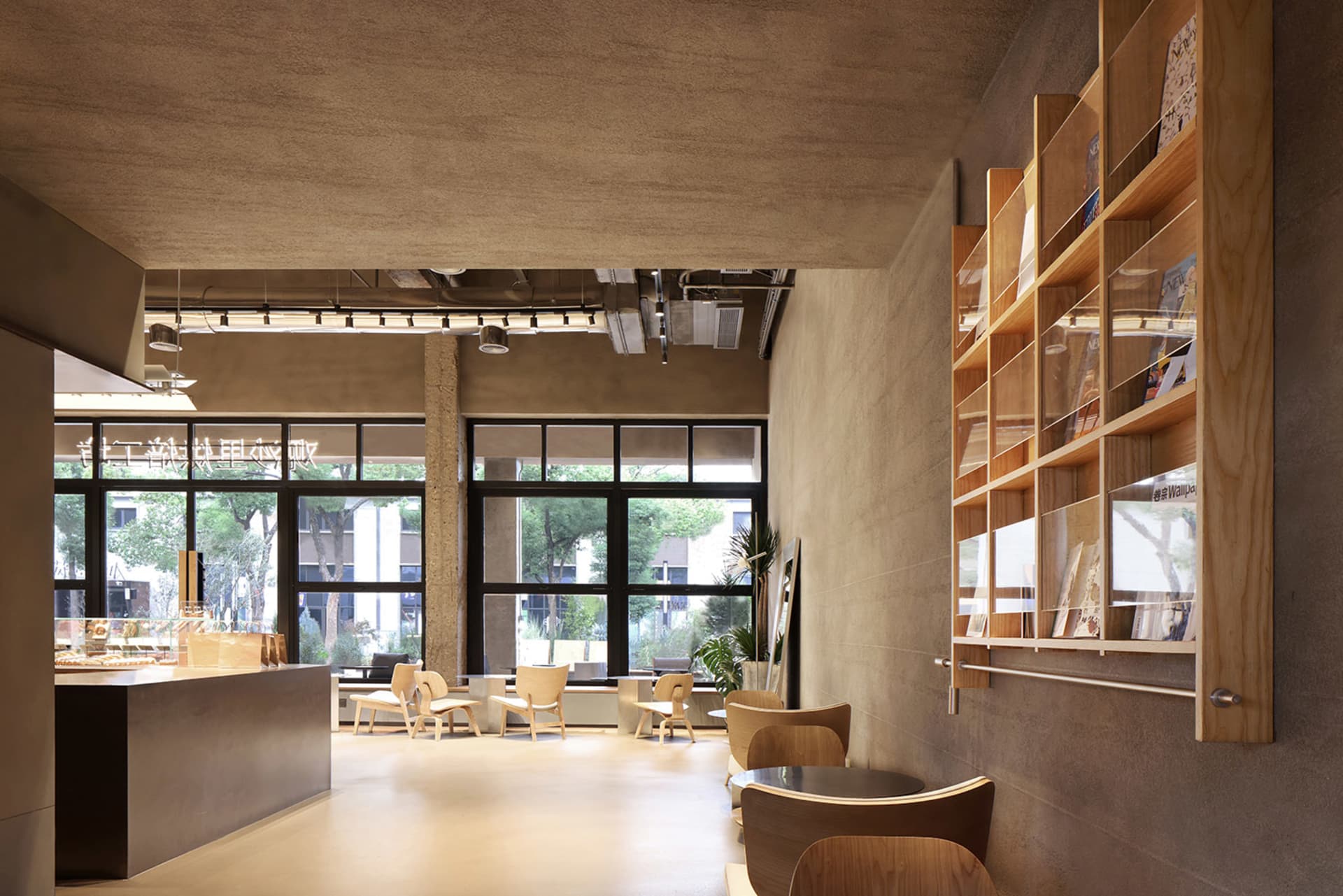 A modern cafe lobby featuring concrete walls, wooden shelves, and glazed cement flooring.