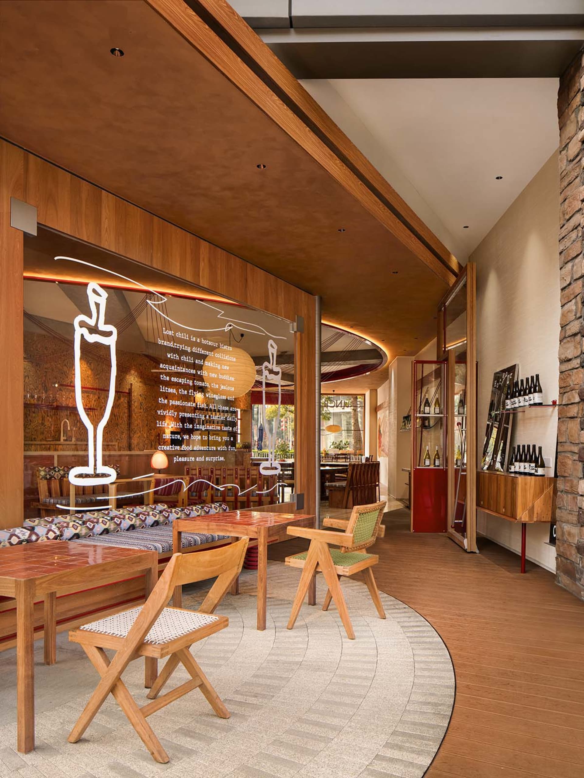 Modern restaurant interior with wooden tables, glass walls, and stone walls.