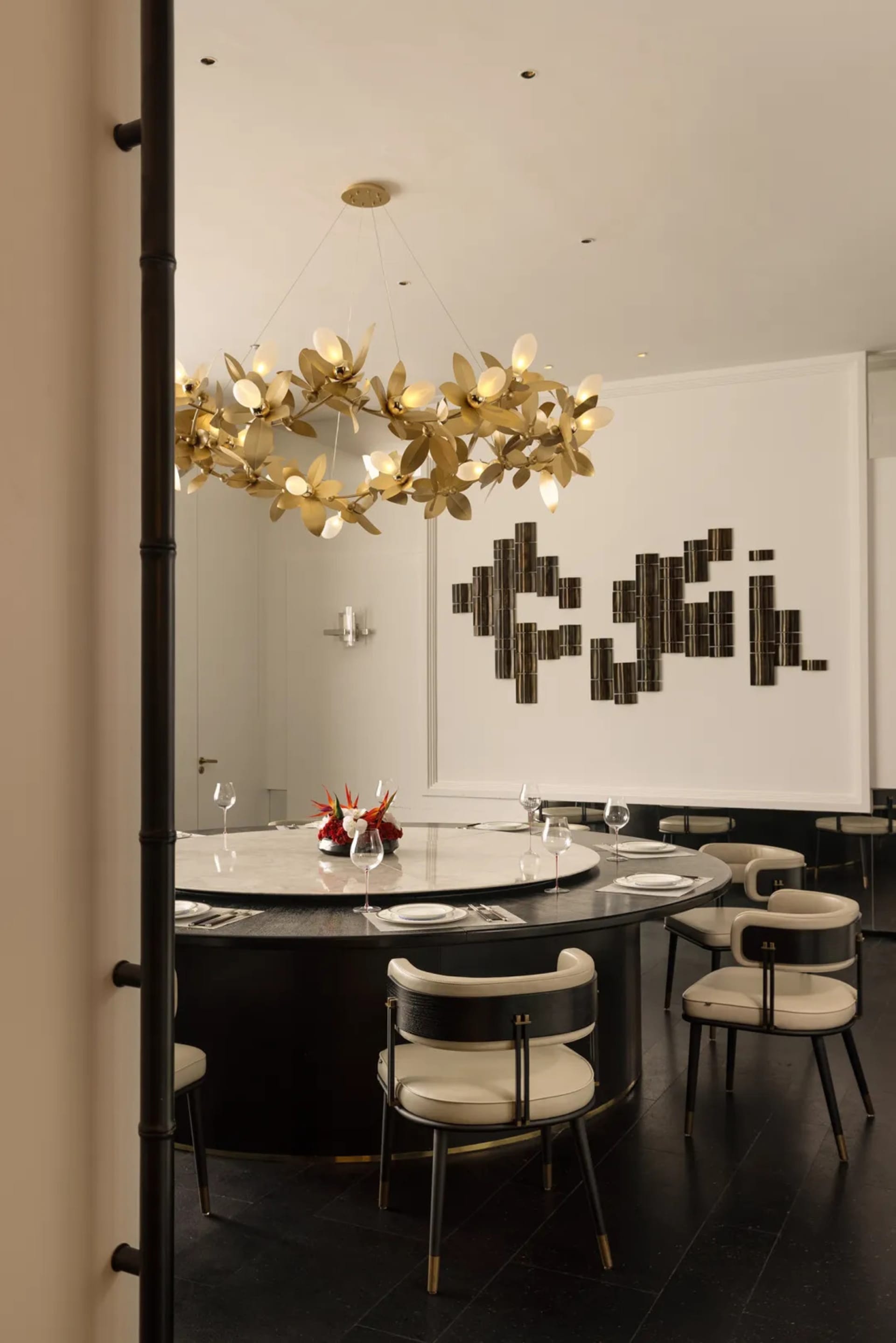 Modern restaurant dining room with metallic chandelier and circular table setup with chairs and wine glasses.