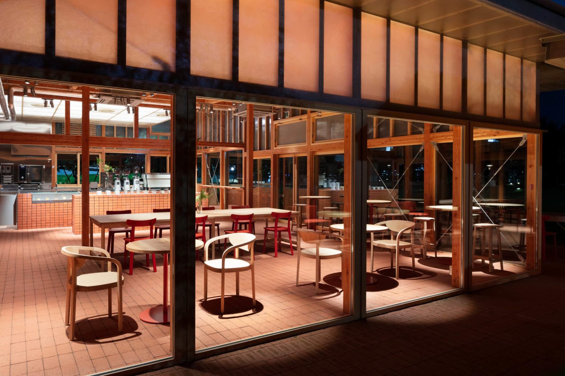 Modern restaurant interior with wooden tables and chairs, glass walls, and exposed beams