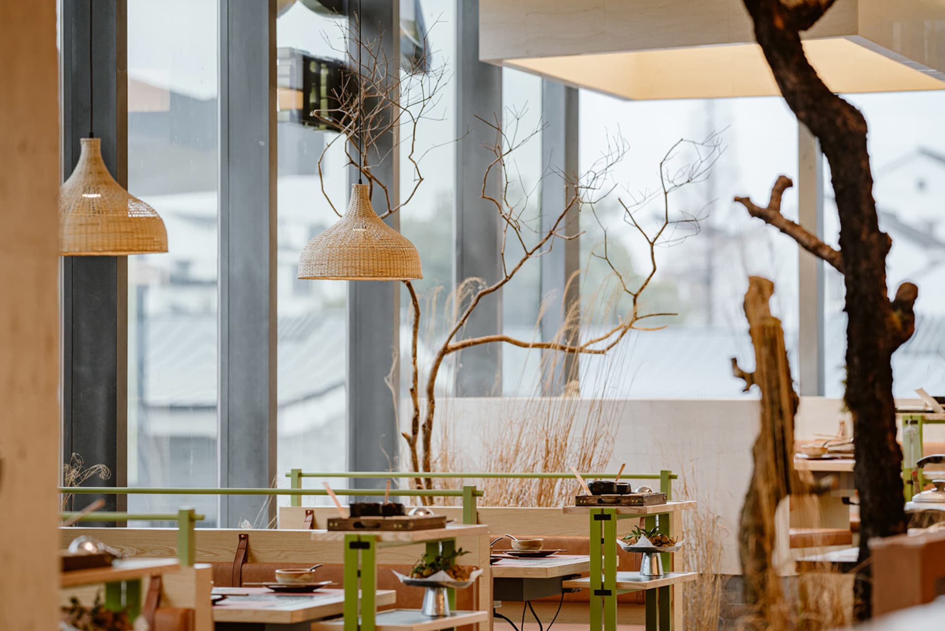Modern restaurant interior with wooden tables, rattan light fixtures, and glass partitions.