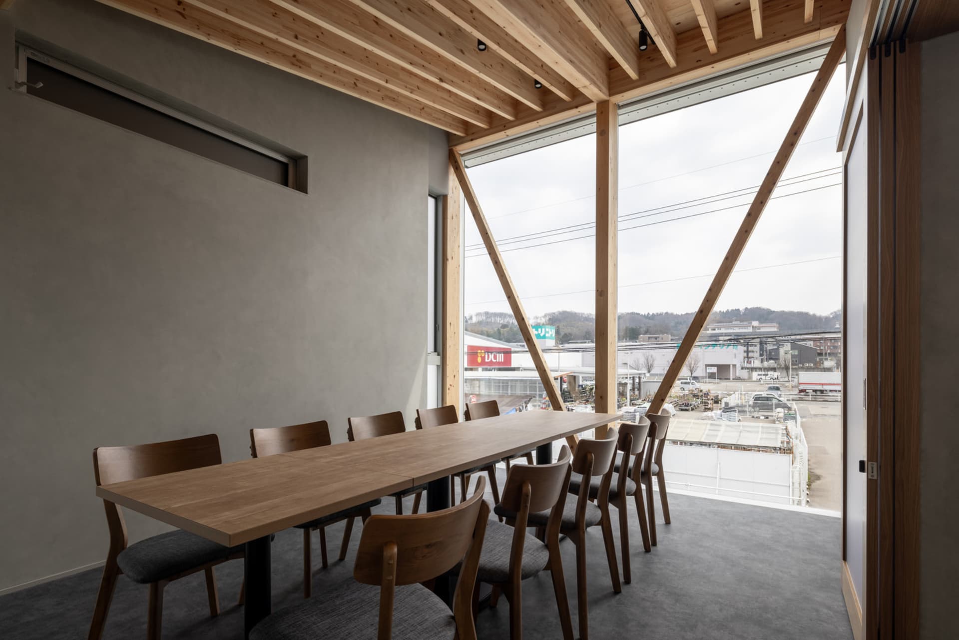 Modern conference room featuring a wooden table and chairs, with a large window providing natural light and a cityscape view.