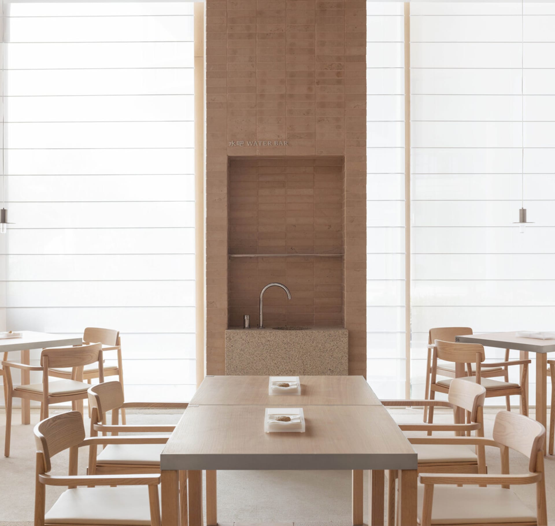 A modern restaurant interior with minimalist design, featuring wooden tables, stone walls, and large windows.