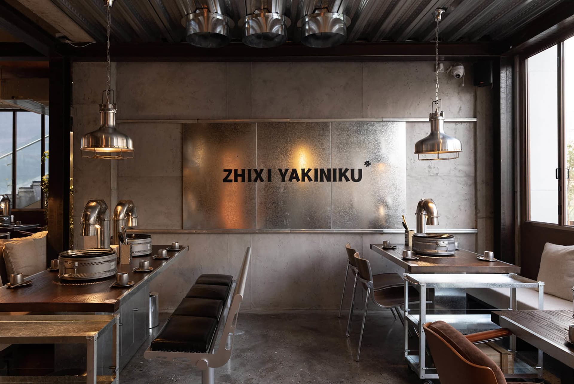 Industrial-style restaurant interior featuring metal and concrete materials, with seating and grills.