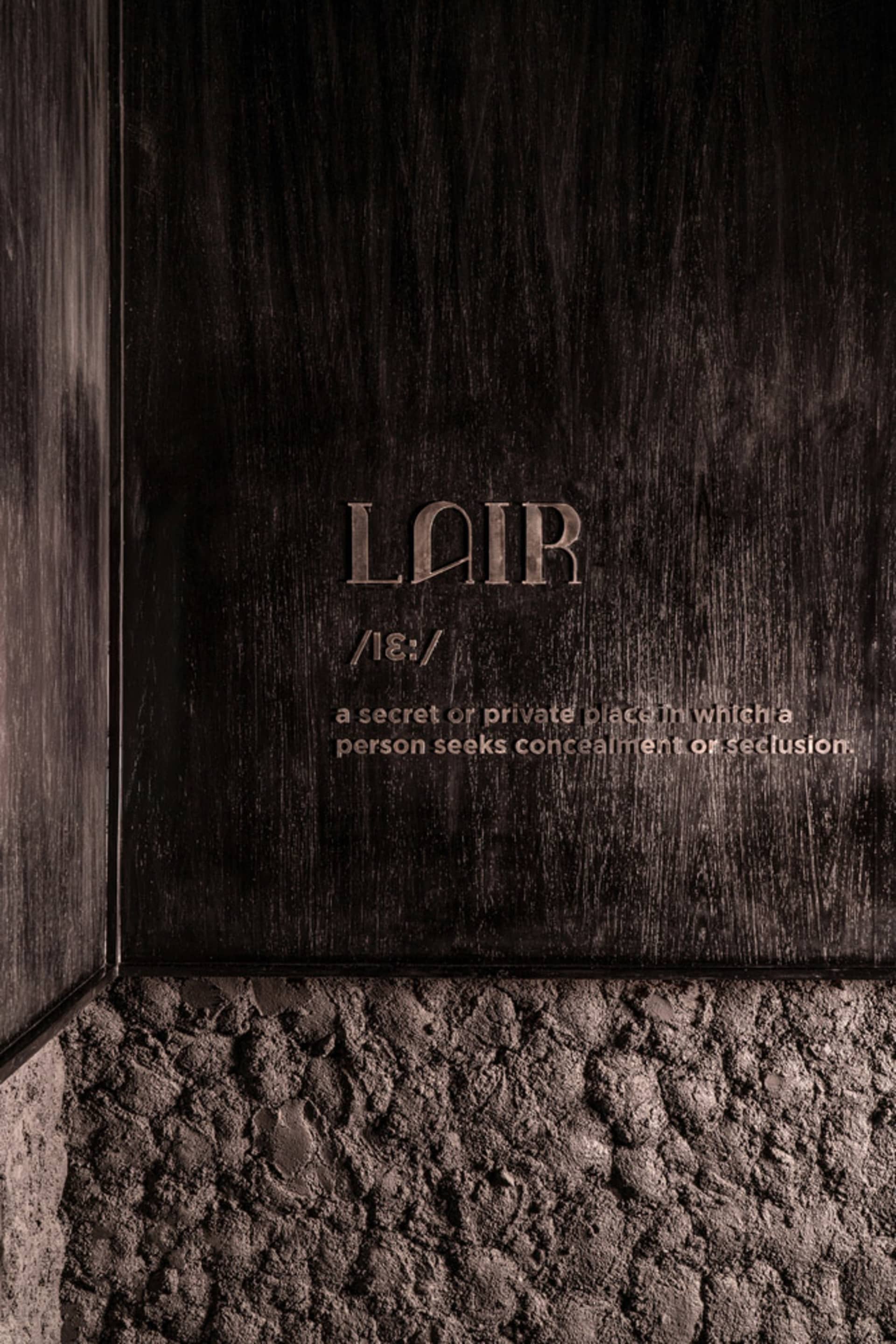 A close-up view of a dark wall interior with wood texture, featuring the word 'Lair' engraved on it.