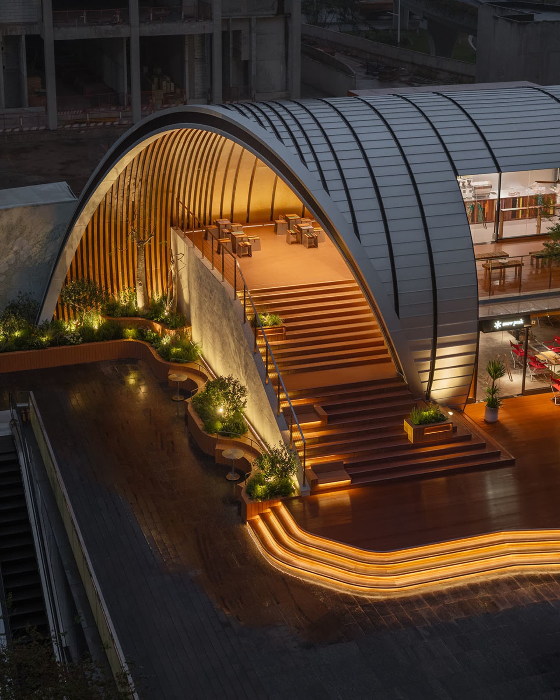 一處帶有金屬建築元素與植物的現代公共空間，燈光照亮。