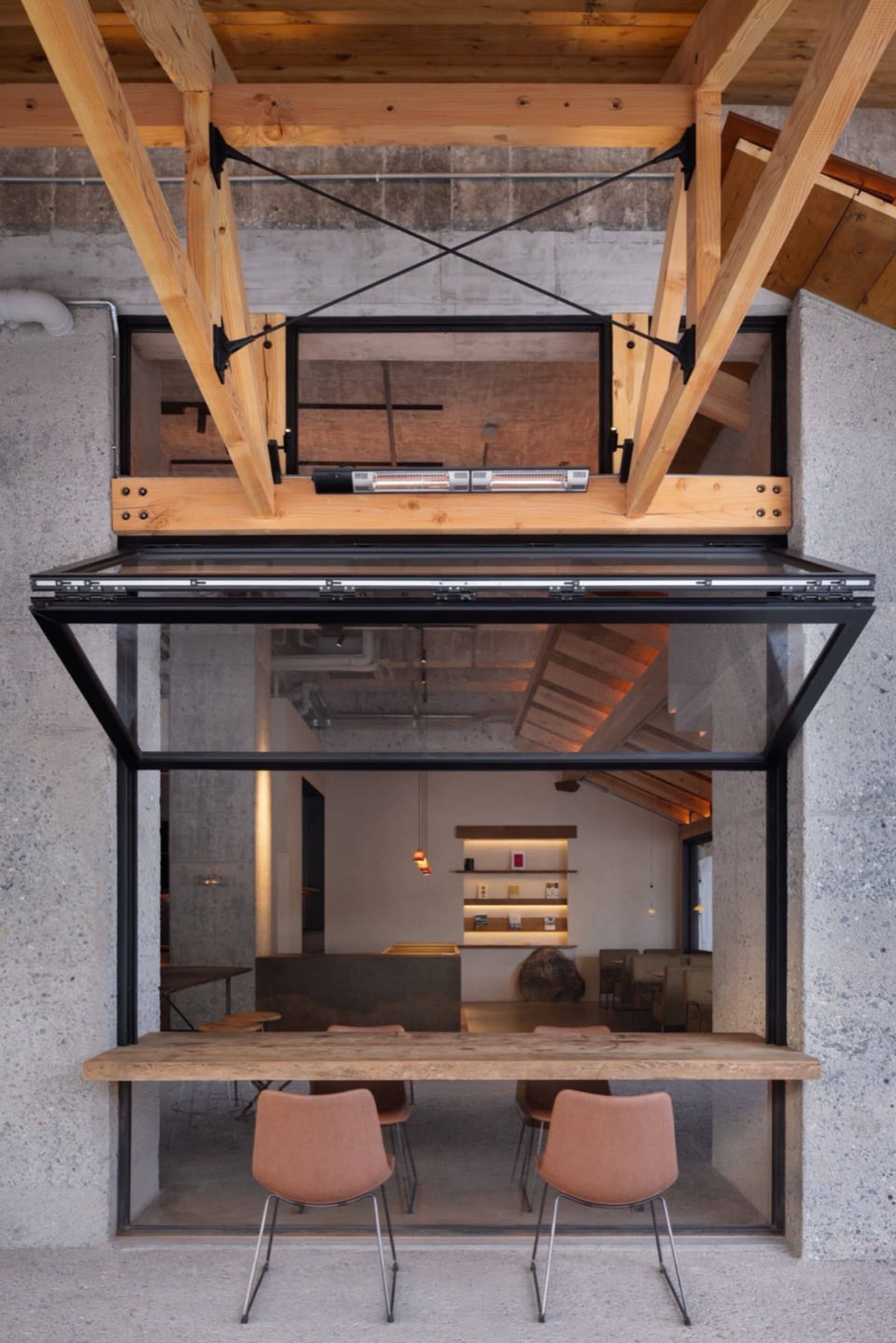 Industrial-style cafe featuring concrete walls, glass windows, and wooden furniture.