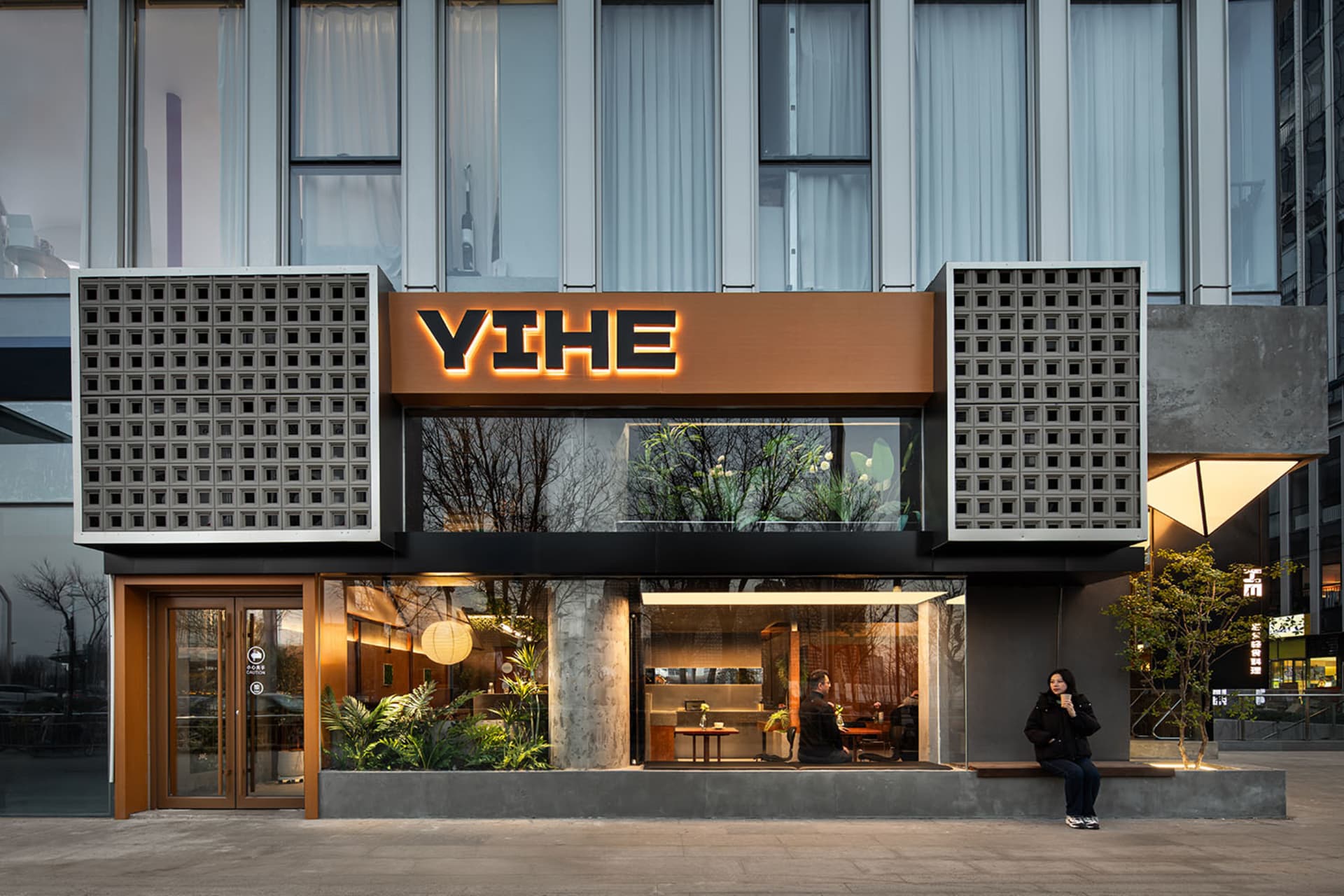 A modern restaurant exterior with a concrete façade and large glass windows.