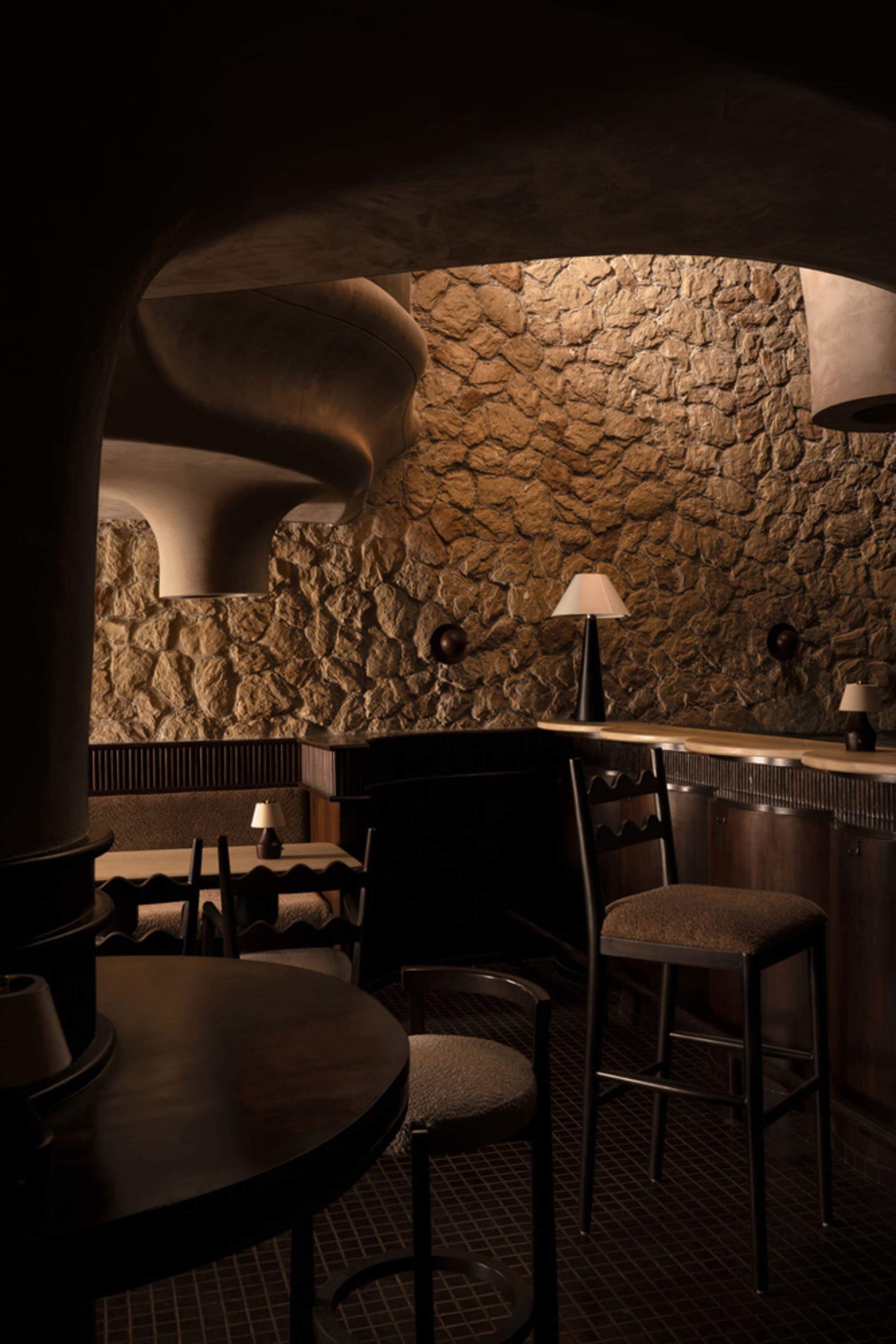 A dimly lit industrial restaurant bar with stone walls and wooden furnishings.