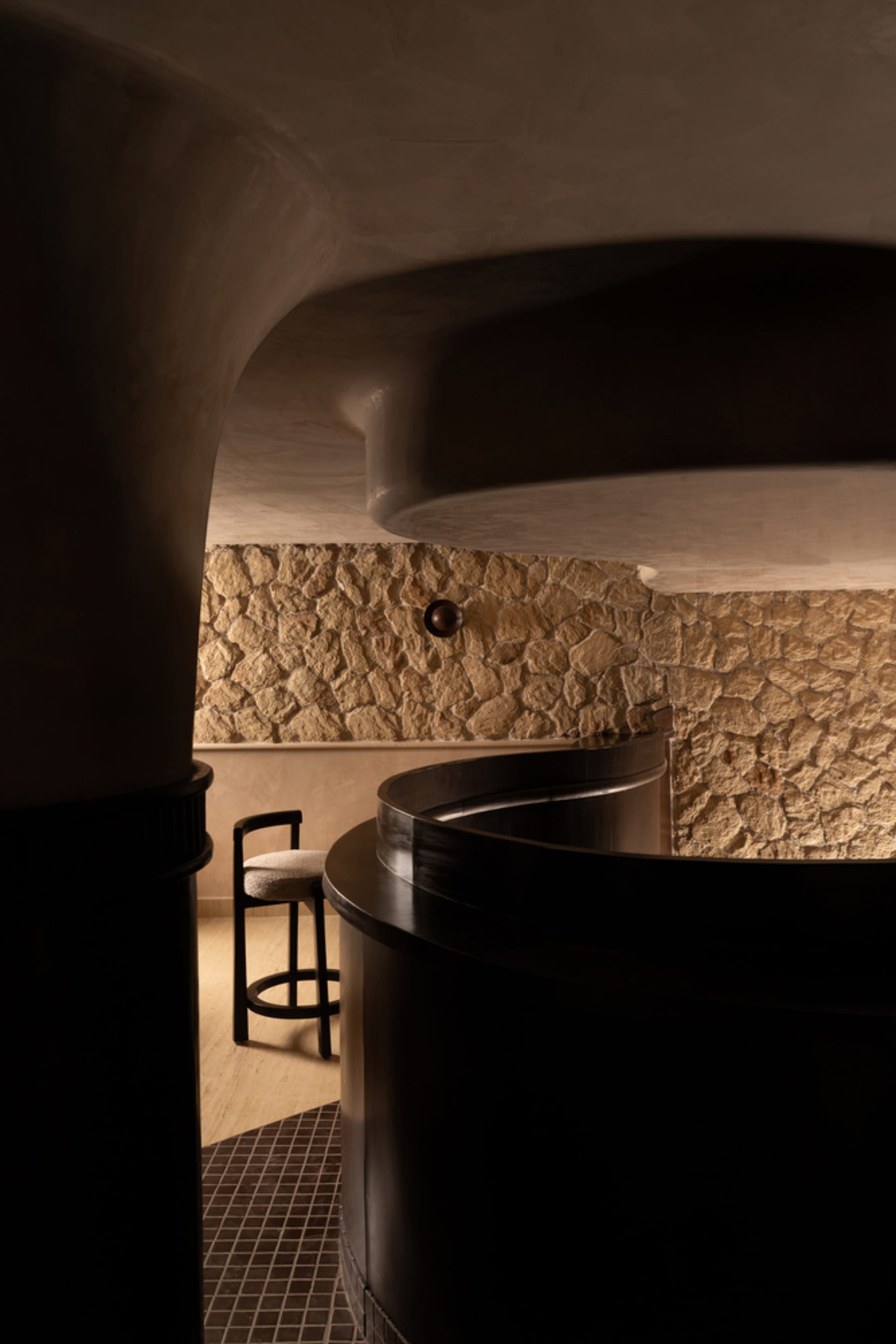 Interior of a modern restaurant featuring a stone wall and a curved metal counter.