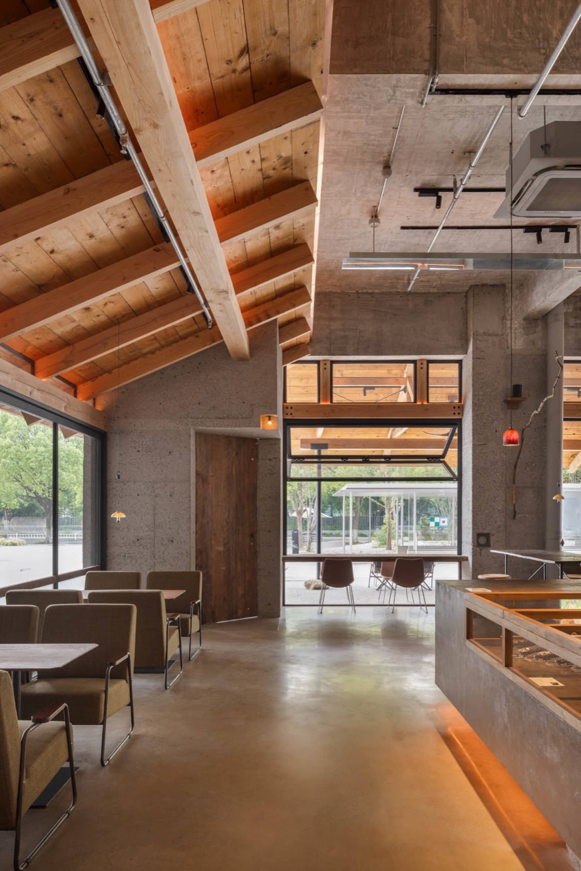 An industrial-style coffee shop interior with concrete walls, wooden elements, and a high ceiling.