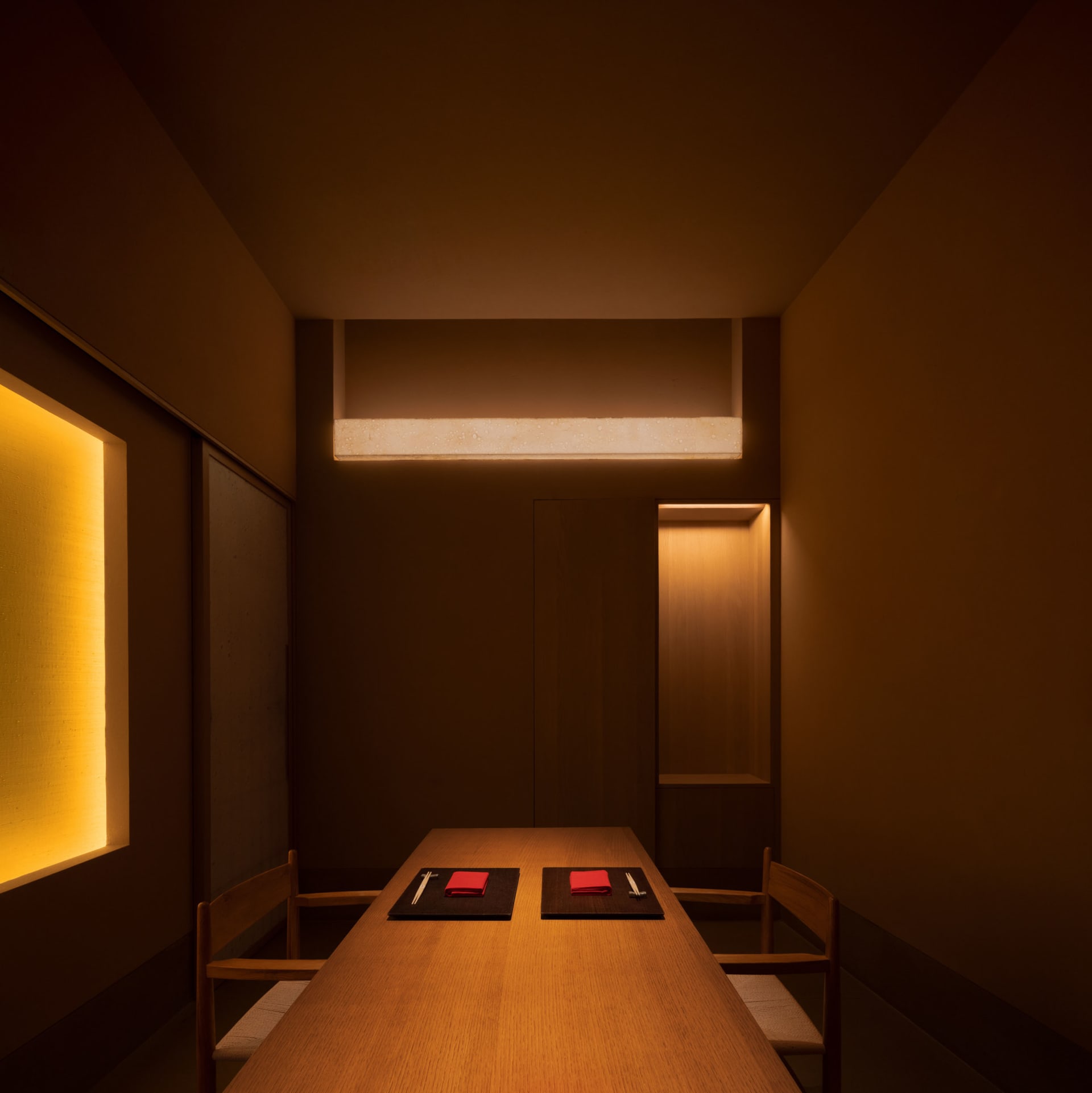 A modern restaurant dining room illuminated by warm, ambient lighting, featuring wooden furniture and minimalist decor.