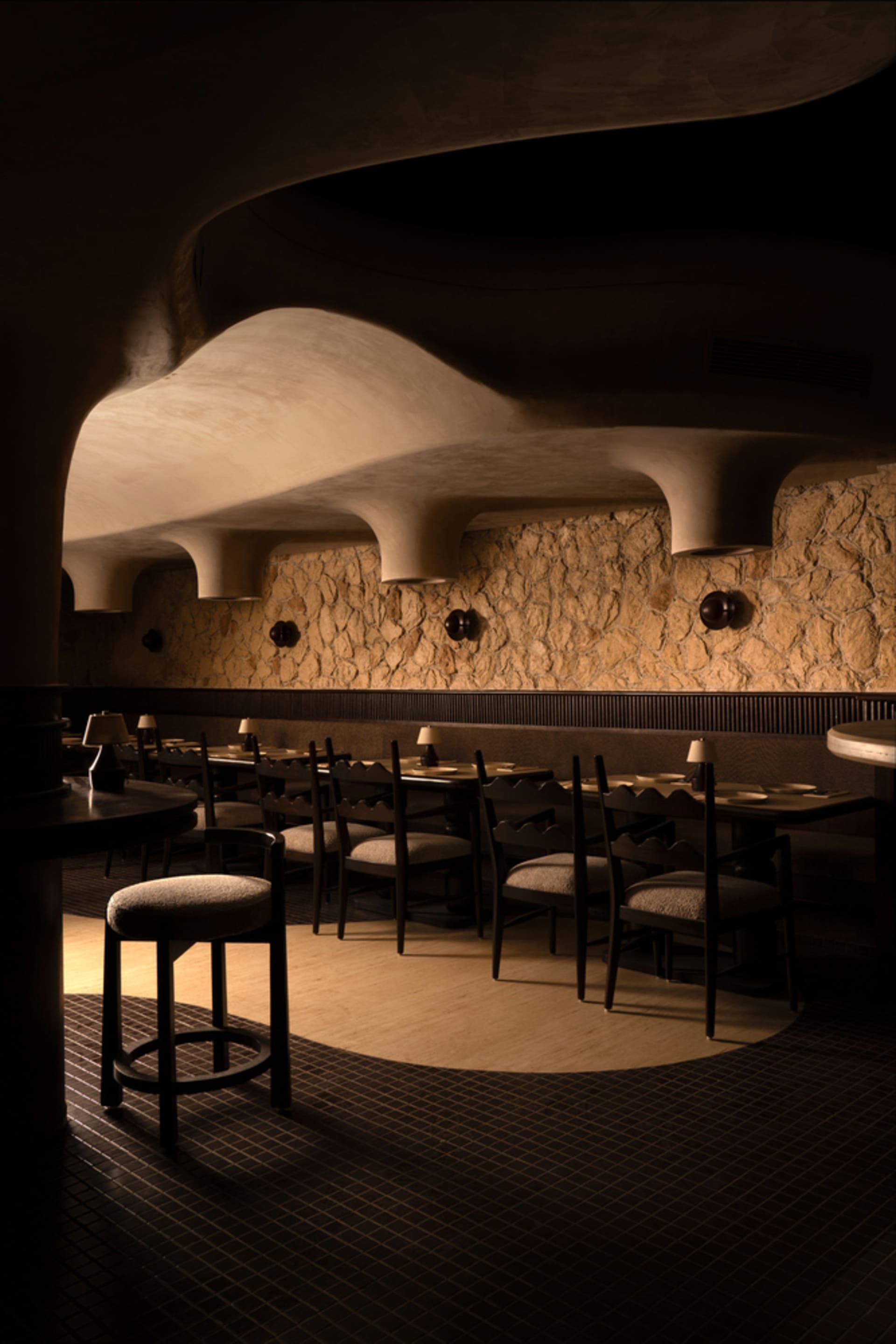 A modern restaurant interior with wooden tables, chairs, and stone walls.