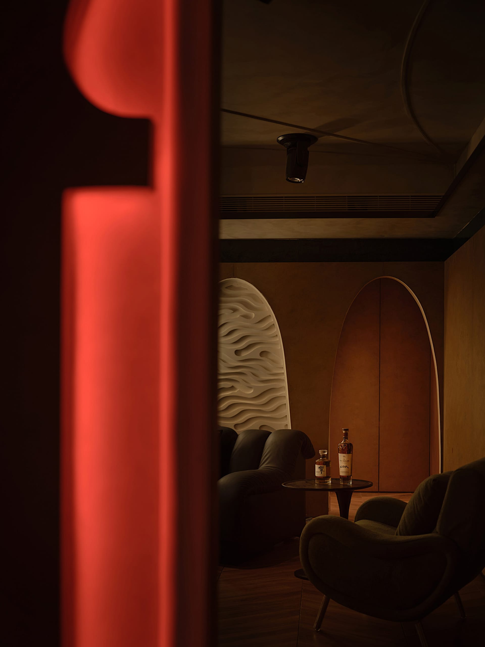 A modern wine bar with wooden paneling, leather armchairs, and upholstered fabric seating.