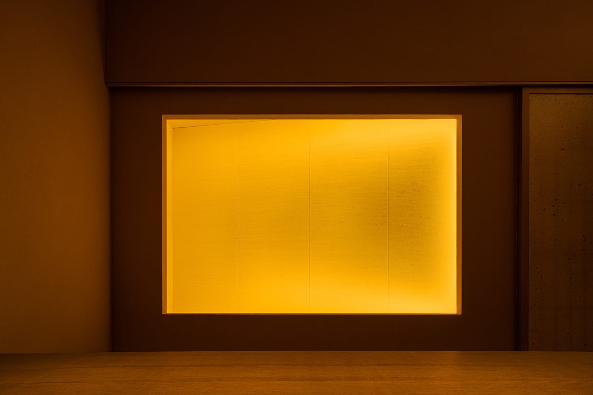Minimalist interior space illuminated with warm, yellow lighting.
