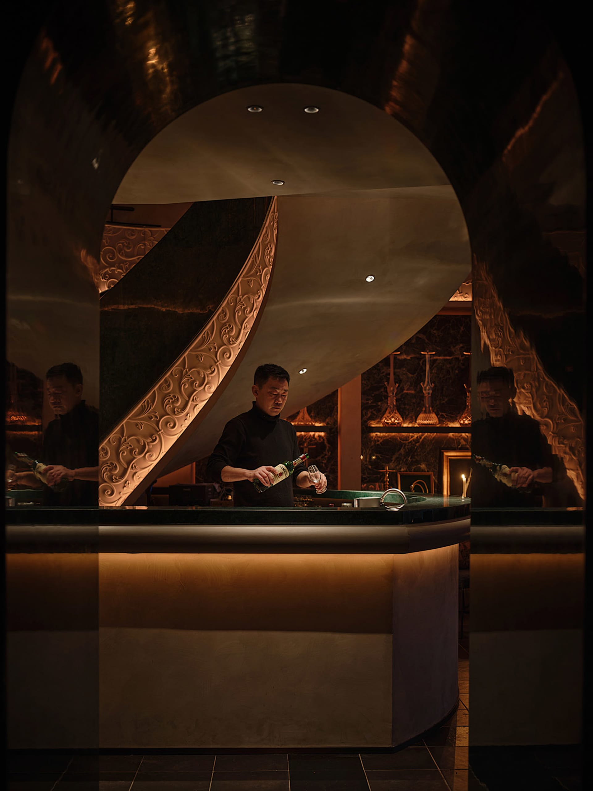 A man pouring a drink into a glass at a modern marble bar counter