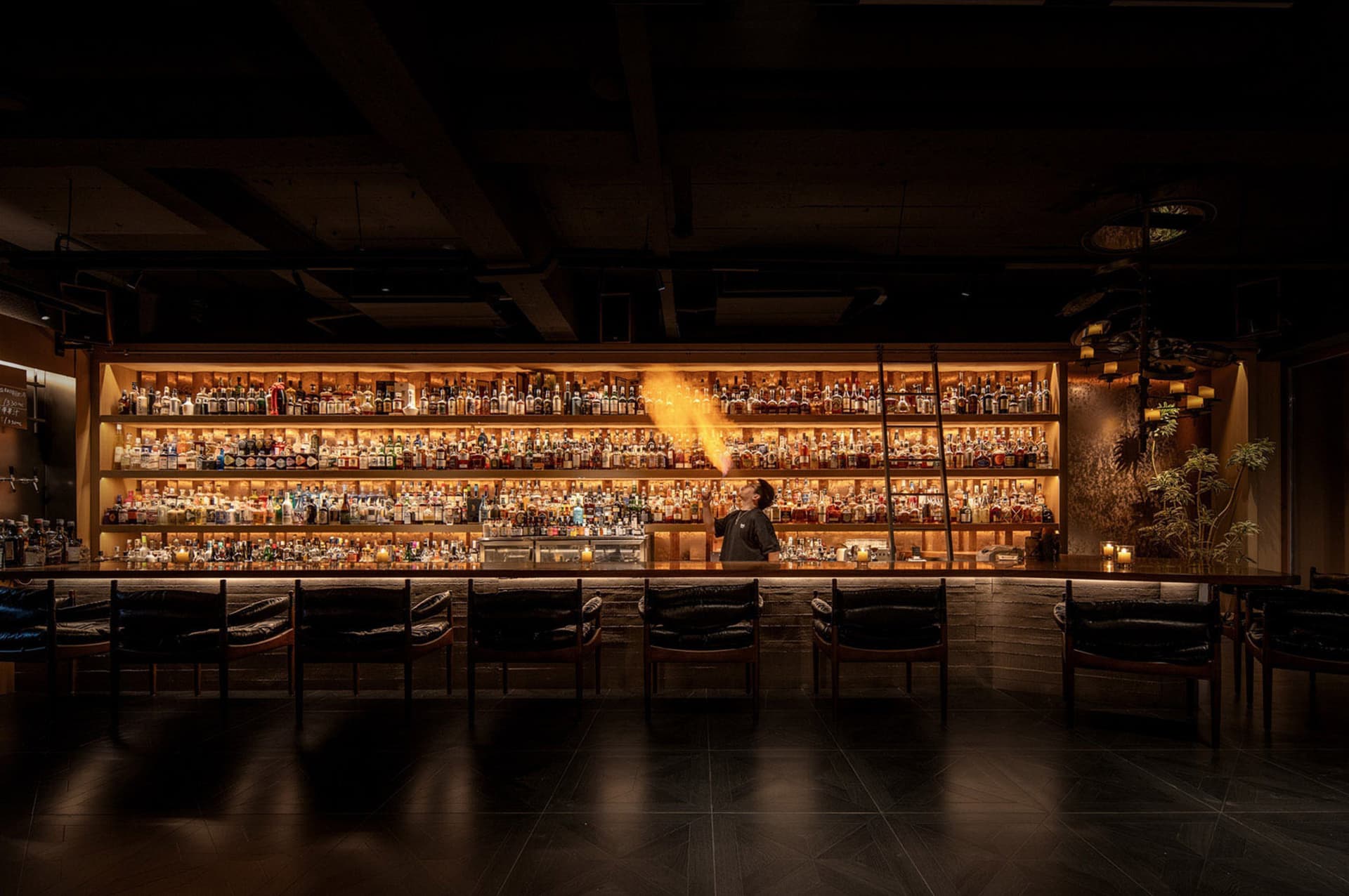 An image of a modern bar interior with a well-stocked bar, dim lighting, and seating.