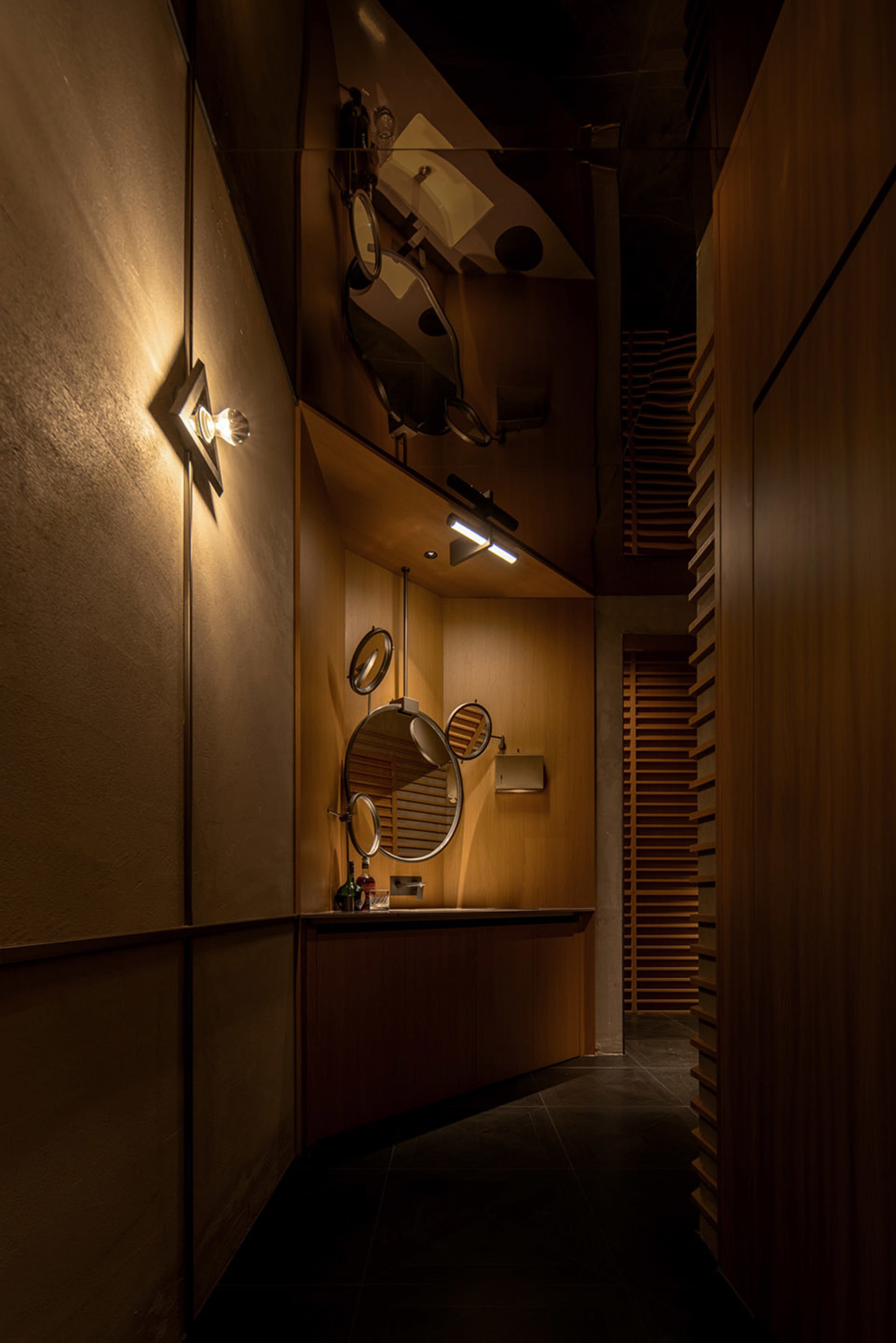 A modern bathroom featuring wooden walls and ceiling with industrial-style wall lights.