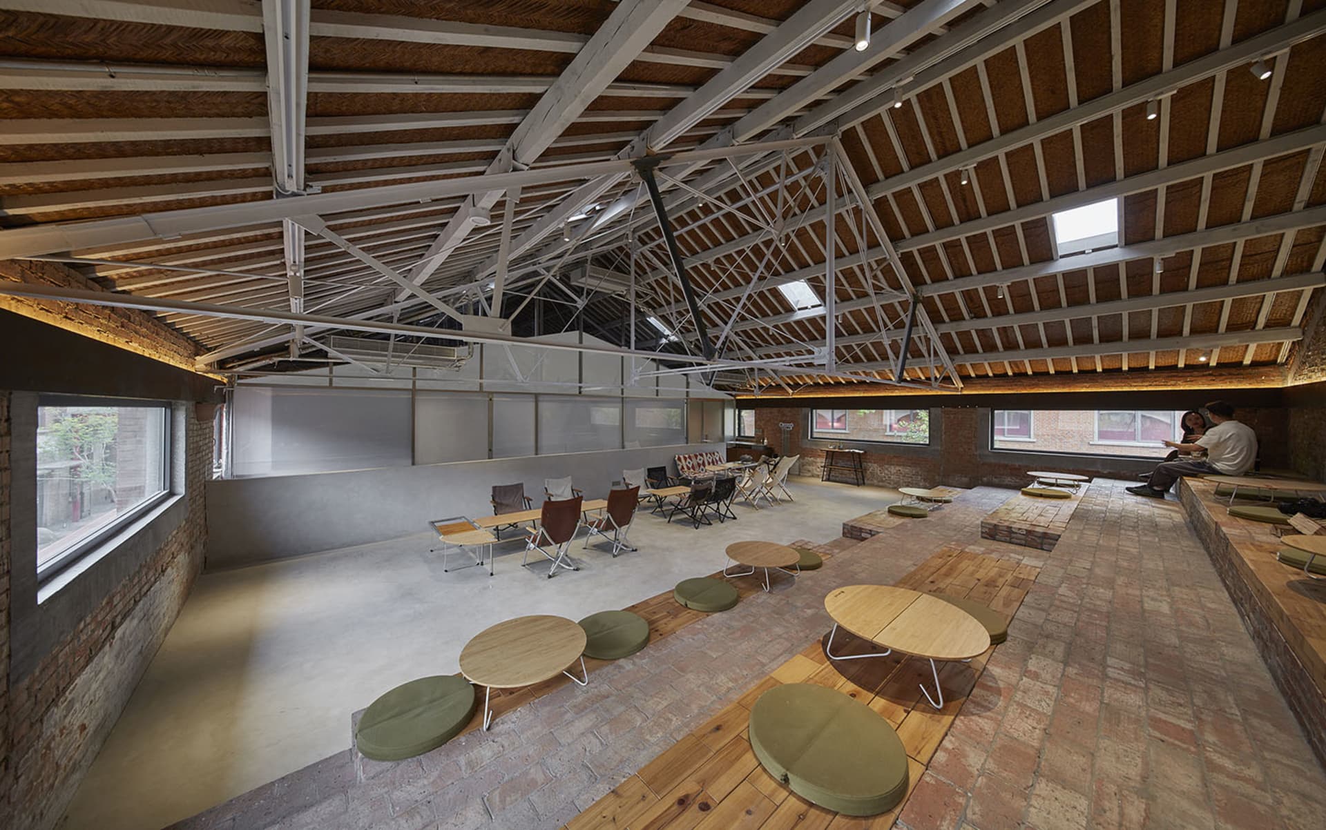 Industrial-style co-working space featuring exposed concrete flooring, brick walls, and rustic wooden furniture.