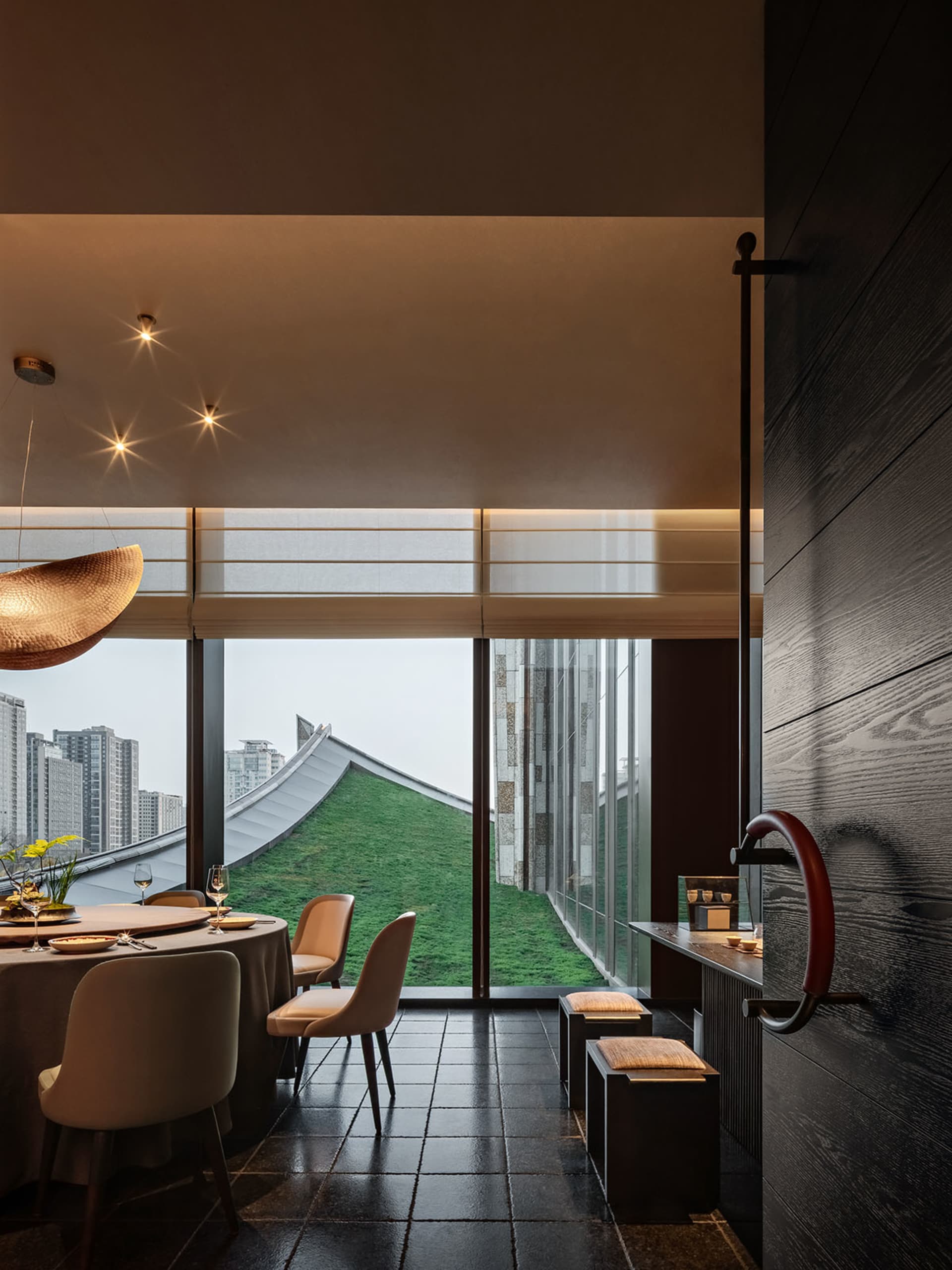 A modern restaurant interior with black lighting, metallic accents, and a rooftop view of the cityscape.