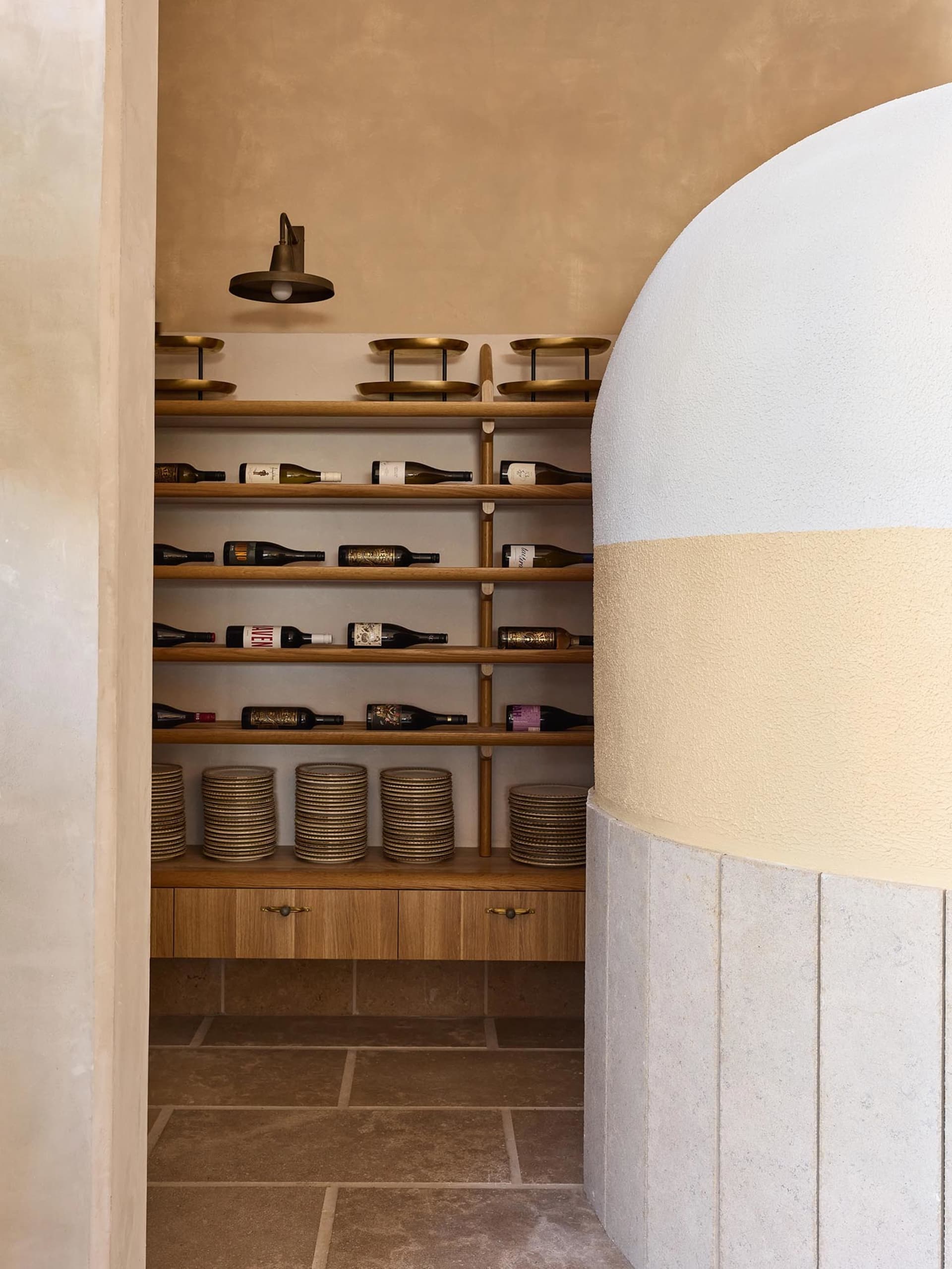 A modern minimalist wine cellar featuring hardwood shelves, stone walls, and concrete flooring.