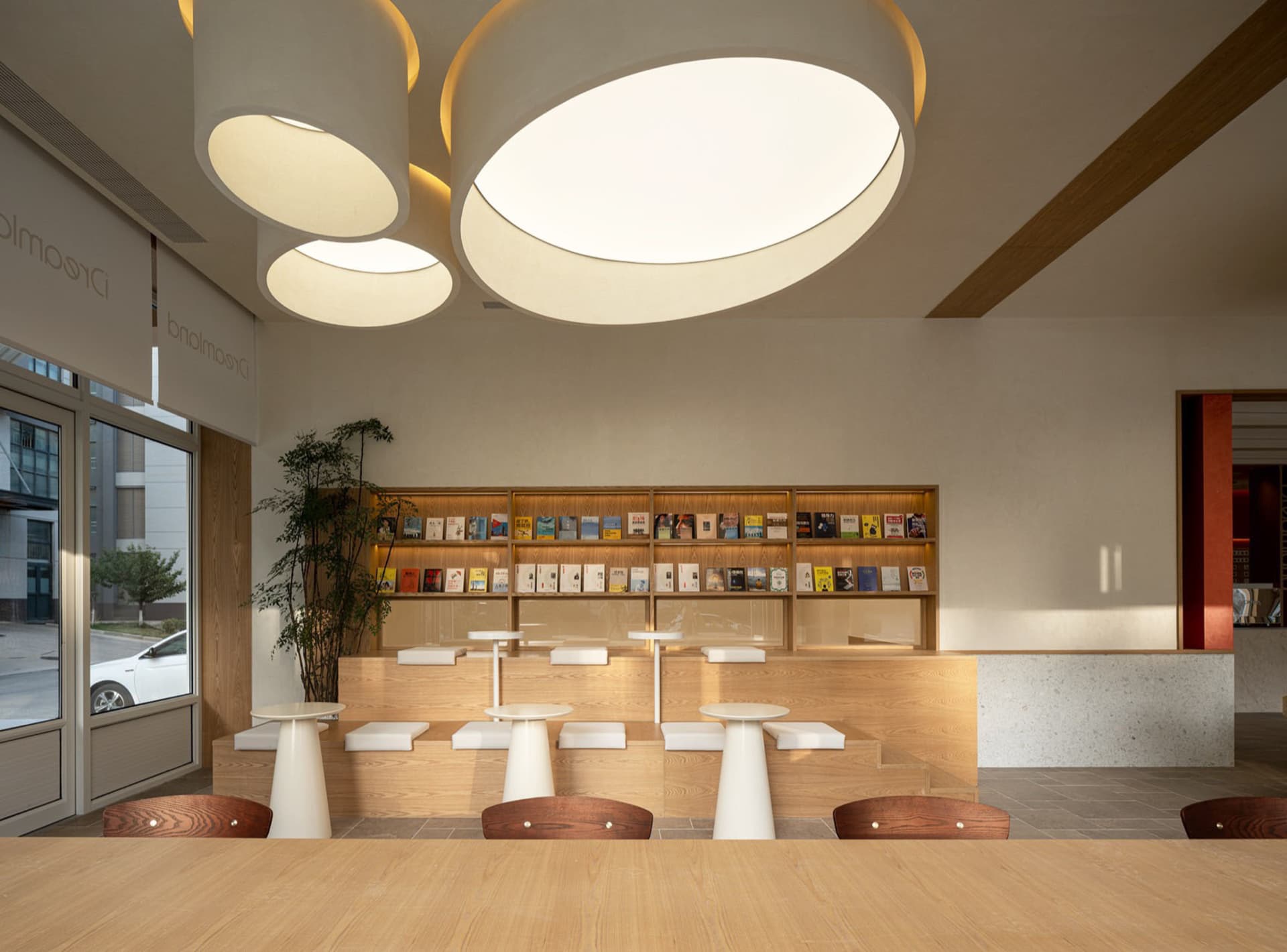 Modern minimalist cafe interior with wood tables, stools, and a round glass dining table.