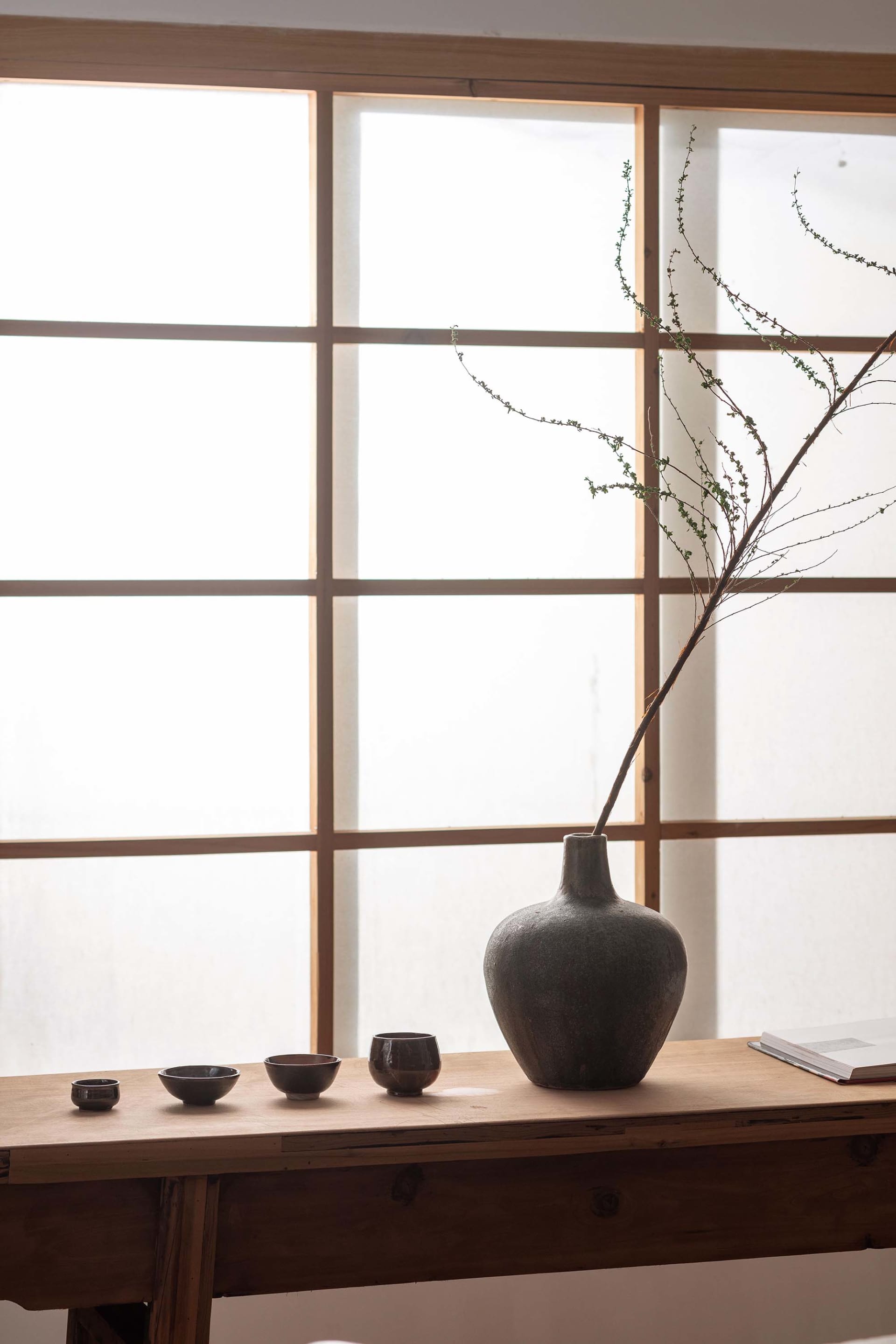 A minimalist vase design placed on a wooden table in front of a Japanese-style shoji window, featuring a natural branch in th