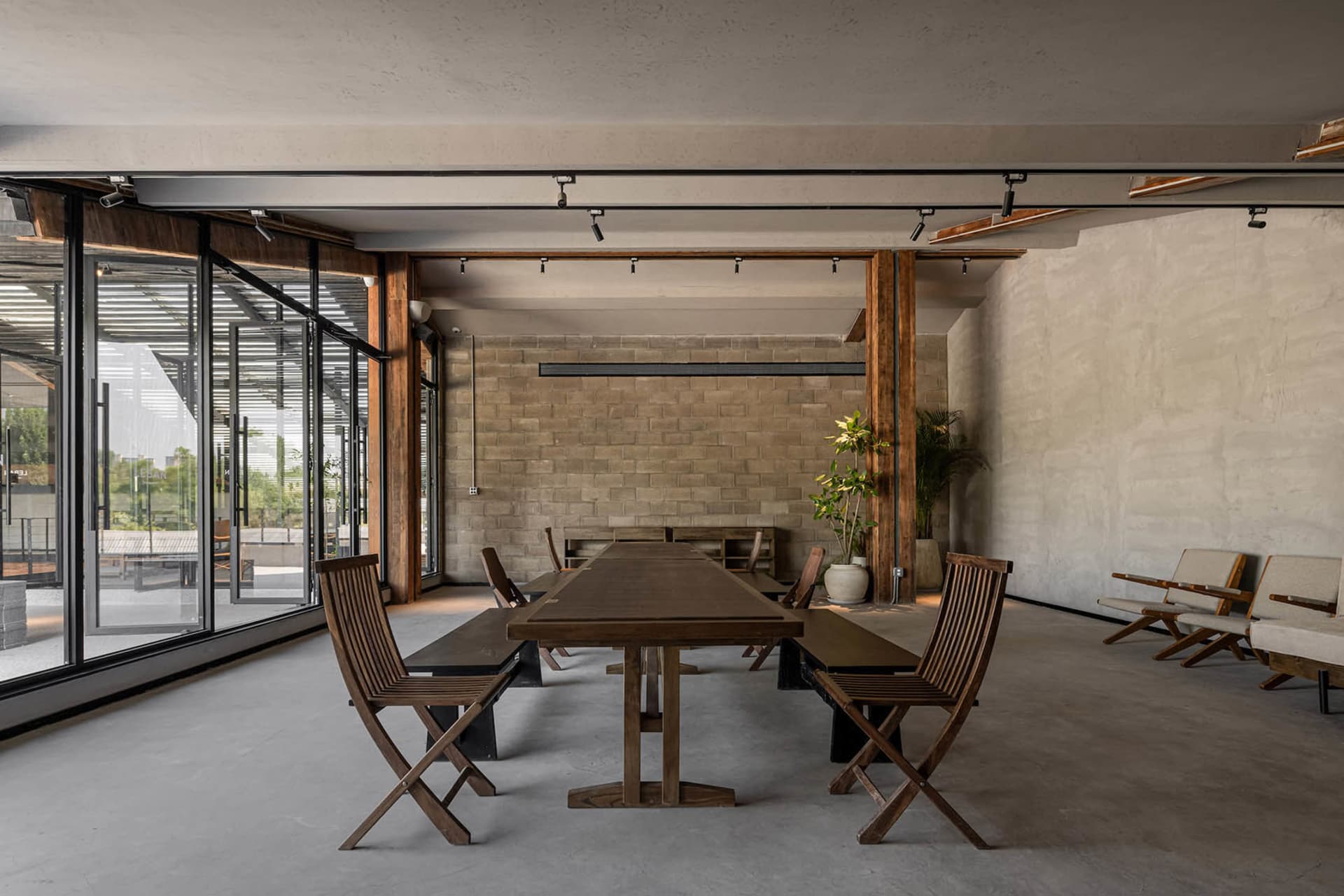 A modern meeting room featuring concrete walls and wooden furniture, with large windows allowing natural light.