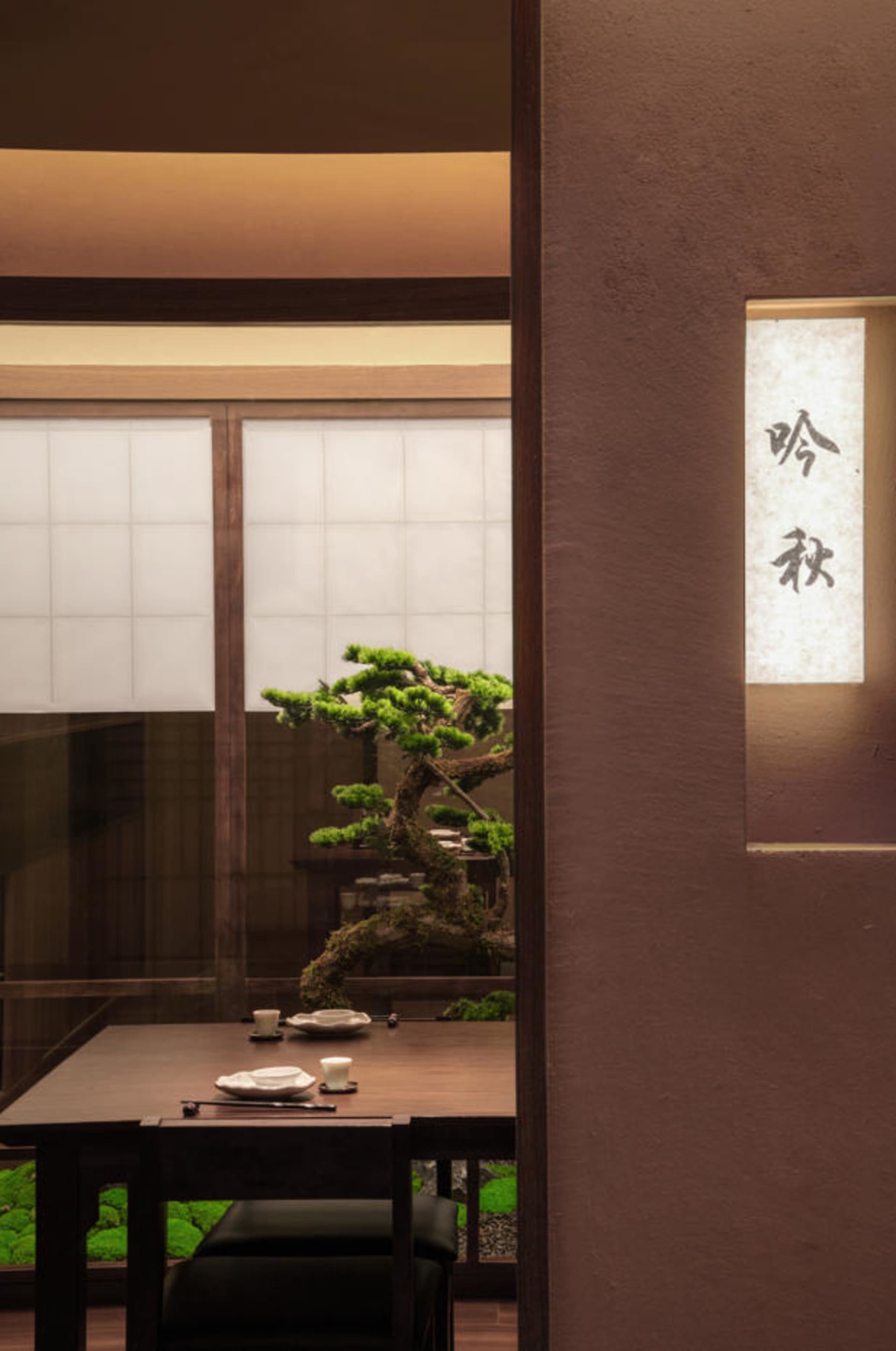 極簡風格的餐廳室內，配有木質餐桌、混凝土地板，以及牆上懸掛的紙燈籠。