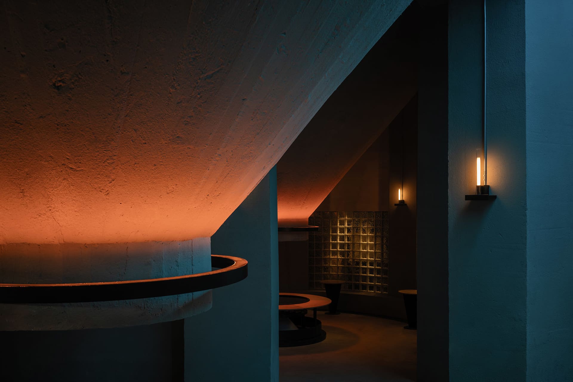 A modern lobby interior featuring exposed concrete walls and a warm, rugged lighting ambiance.