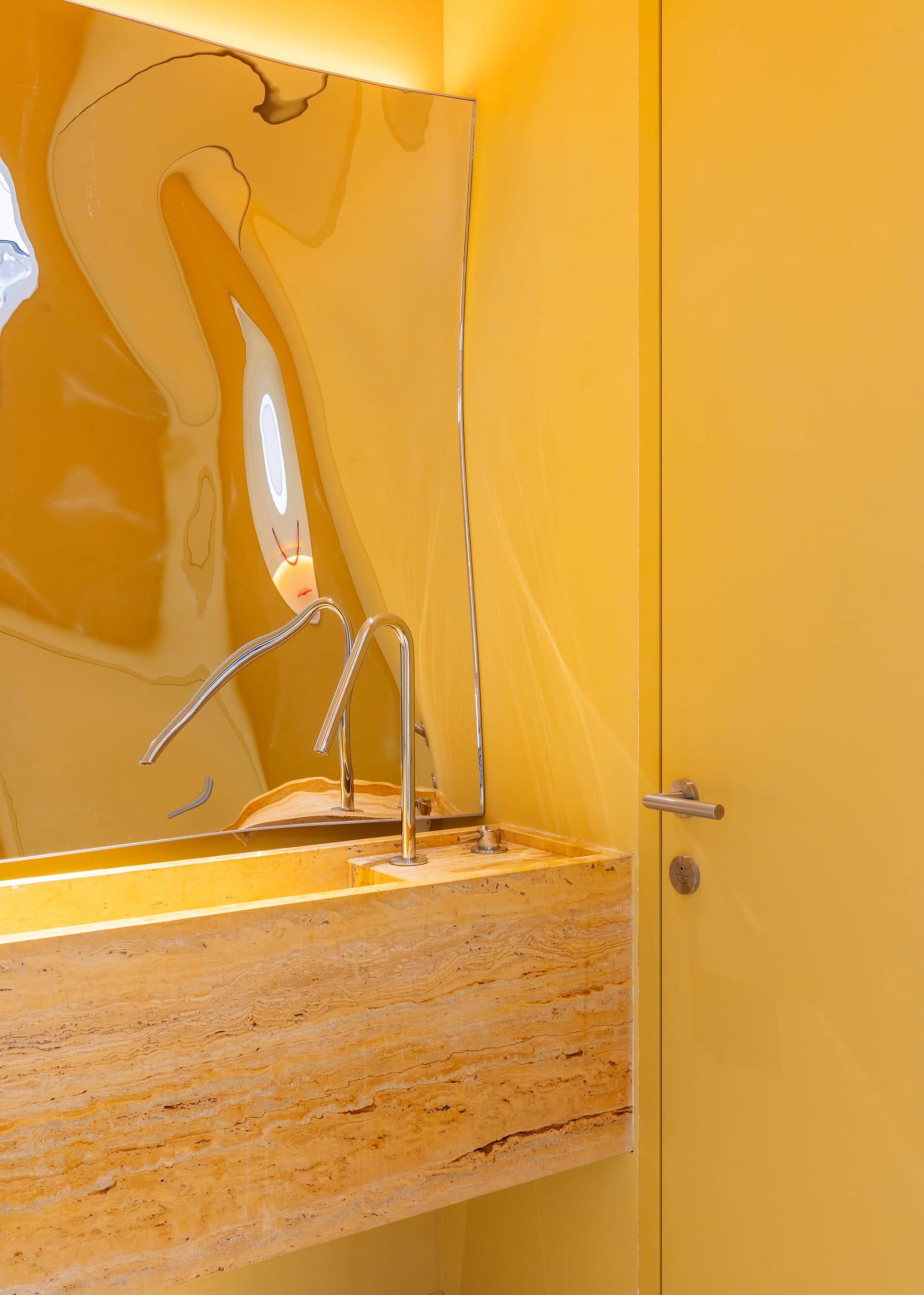 Modern marble bathroom with a yellow wall and a unique, abstract mirror.