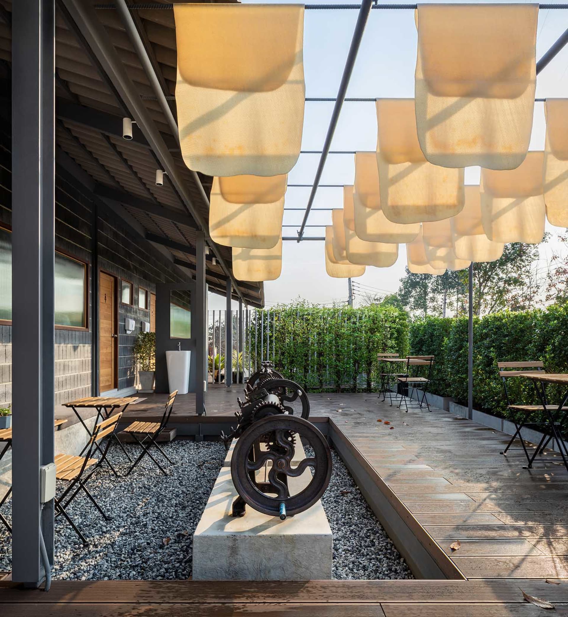 An industrial-style outdoor seating area with fabric canopies, wooden chairs, and concrete flooring.