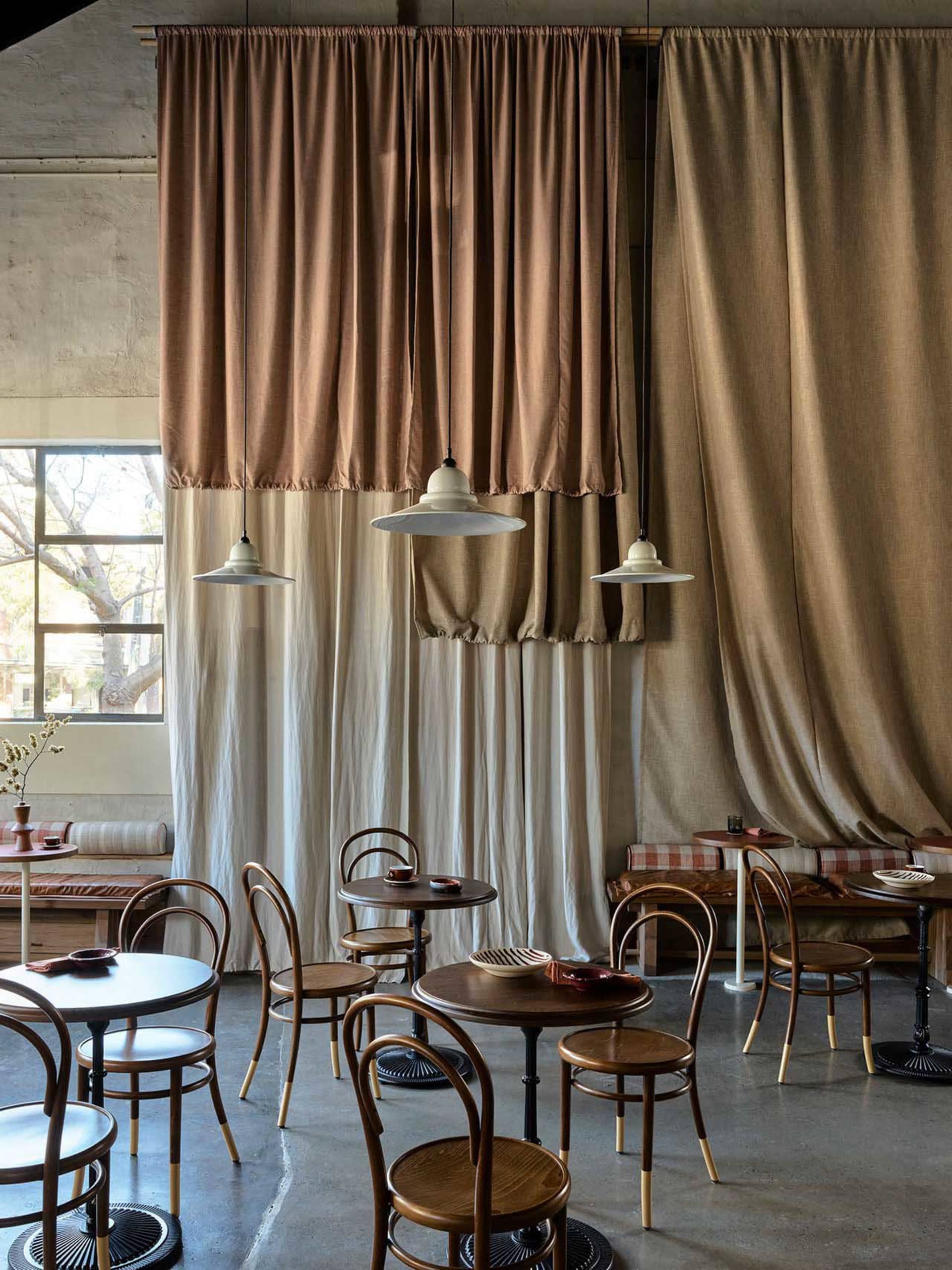 Industrial cafe interior with fabric curtains, wooden tables, and metal pendant lights.