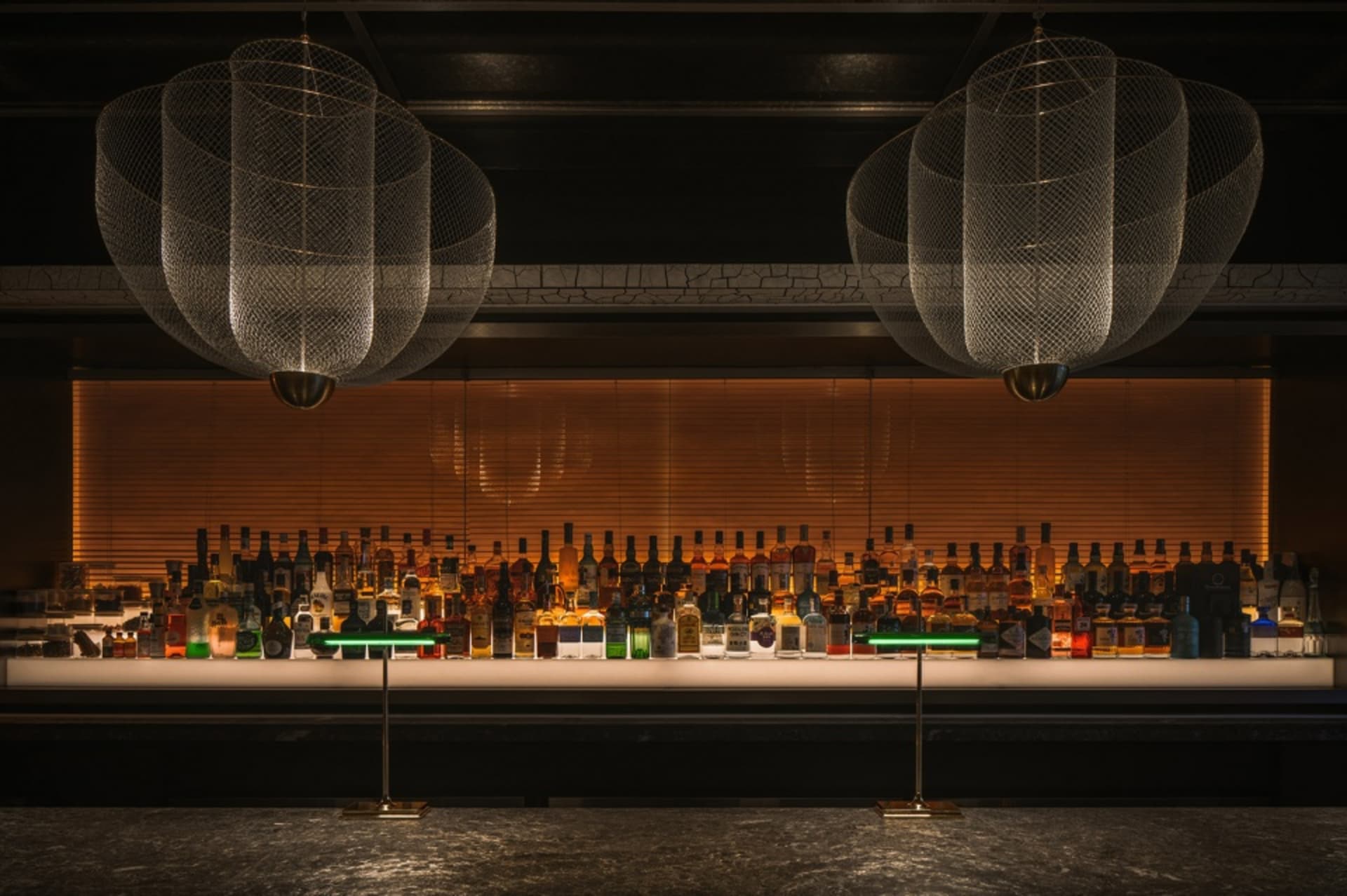 An industrial style bar interior with metal pendant lights, glass bottles, and wooden accents.